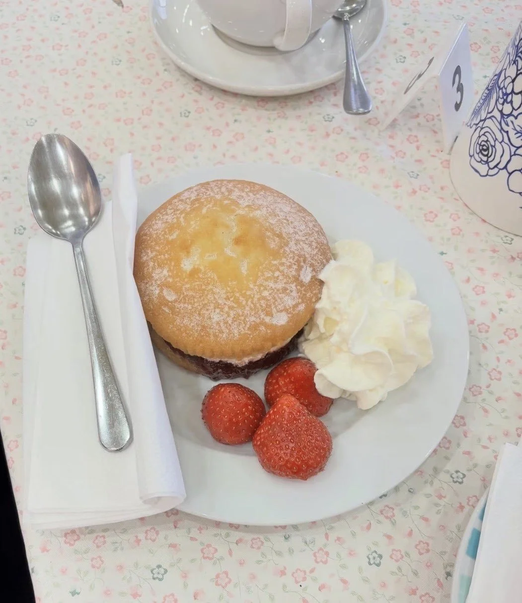 A plate with a baked apple dessert topped with powdered sugar, accompanied by strawberries and whipped cream, on a floral tablecloth.