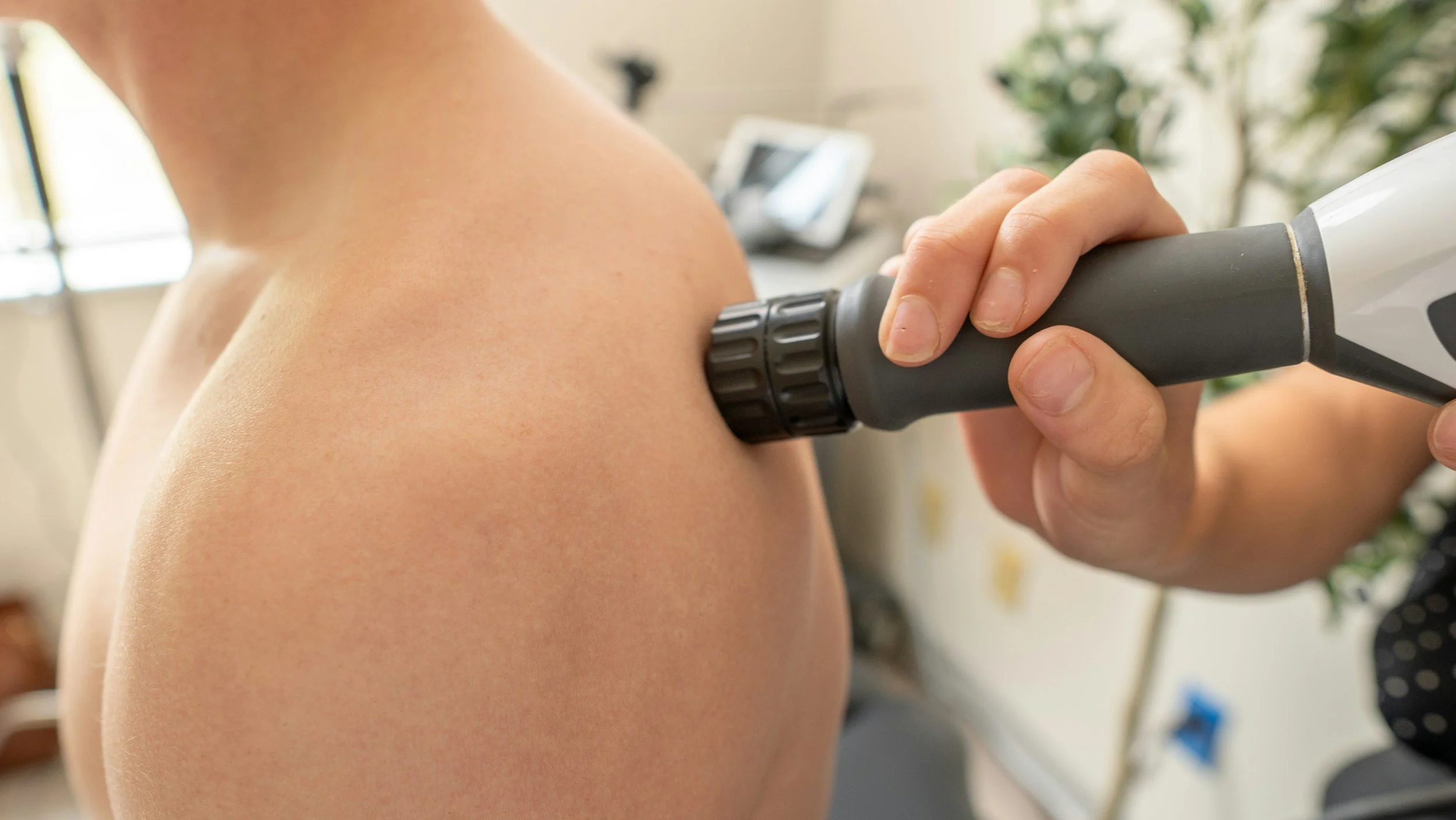 Person using a handheld device on their shoulder in a room with a blurred background.