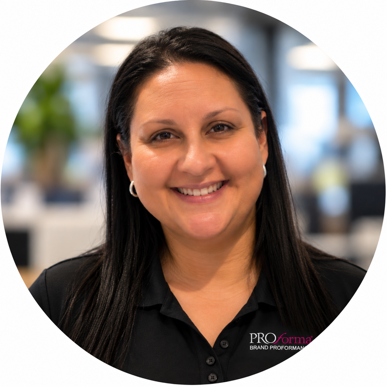 A woman with long dark hair smiling indoors, wearing a black polo shirt with a logo that reads 'PROforma Brand Proformation'.