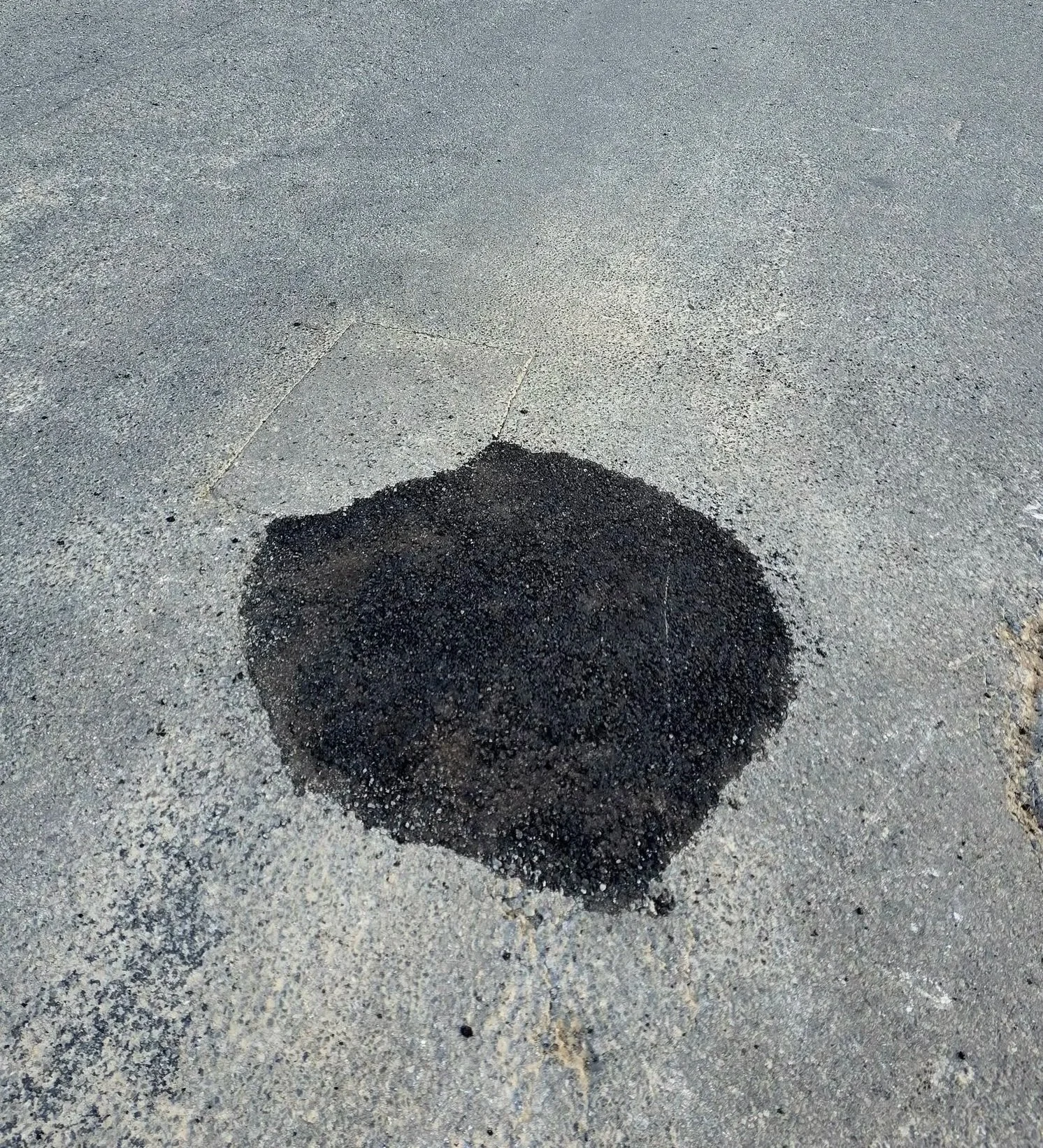 A dark square patch of asphalt on a light gray concrete sidewalk.