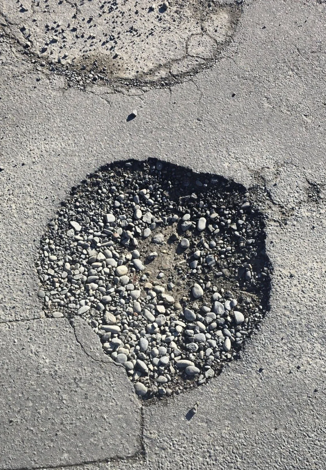 Close-up of a damaged concrete sidewalk with a large hole filled with small gray and white pebbles.