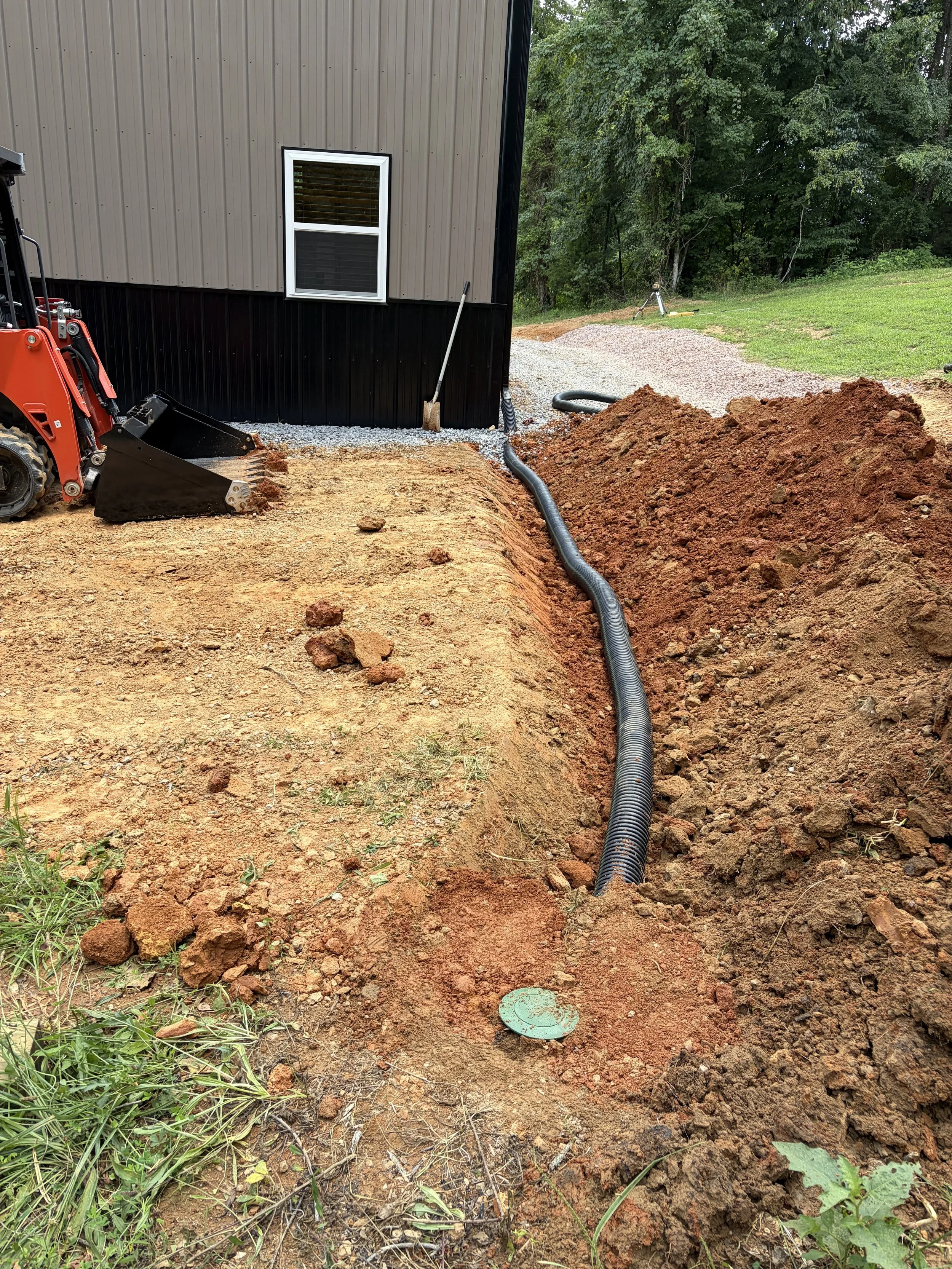 Construction site near Johnson City in East Tennessee with a trench dug around a house foundation, a black drainage pipe installed in the trench, orange excavator on the left.