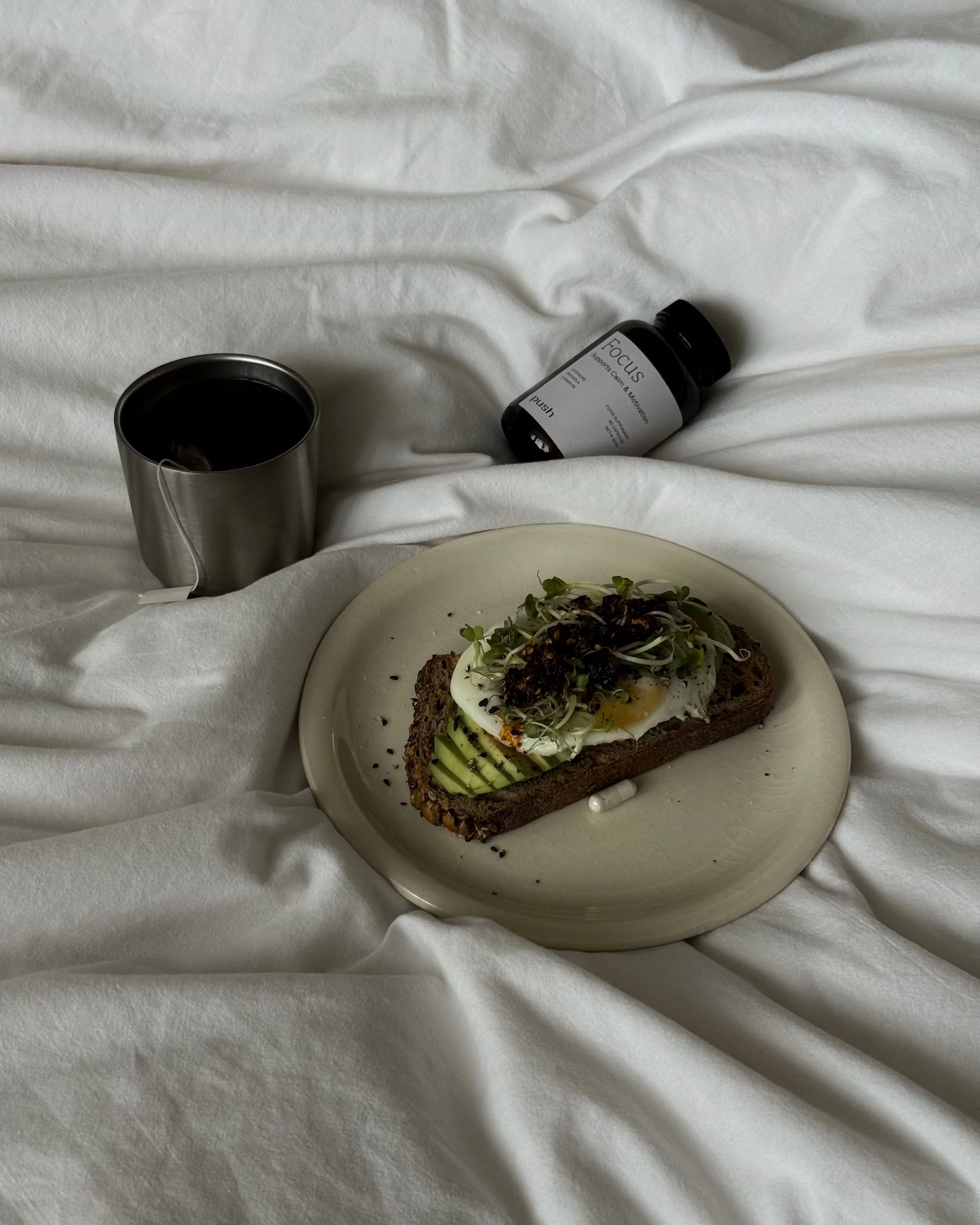 Healthy breakfast with avocado toast, tea and wellness supplements on a bed.