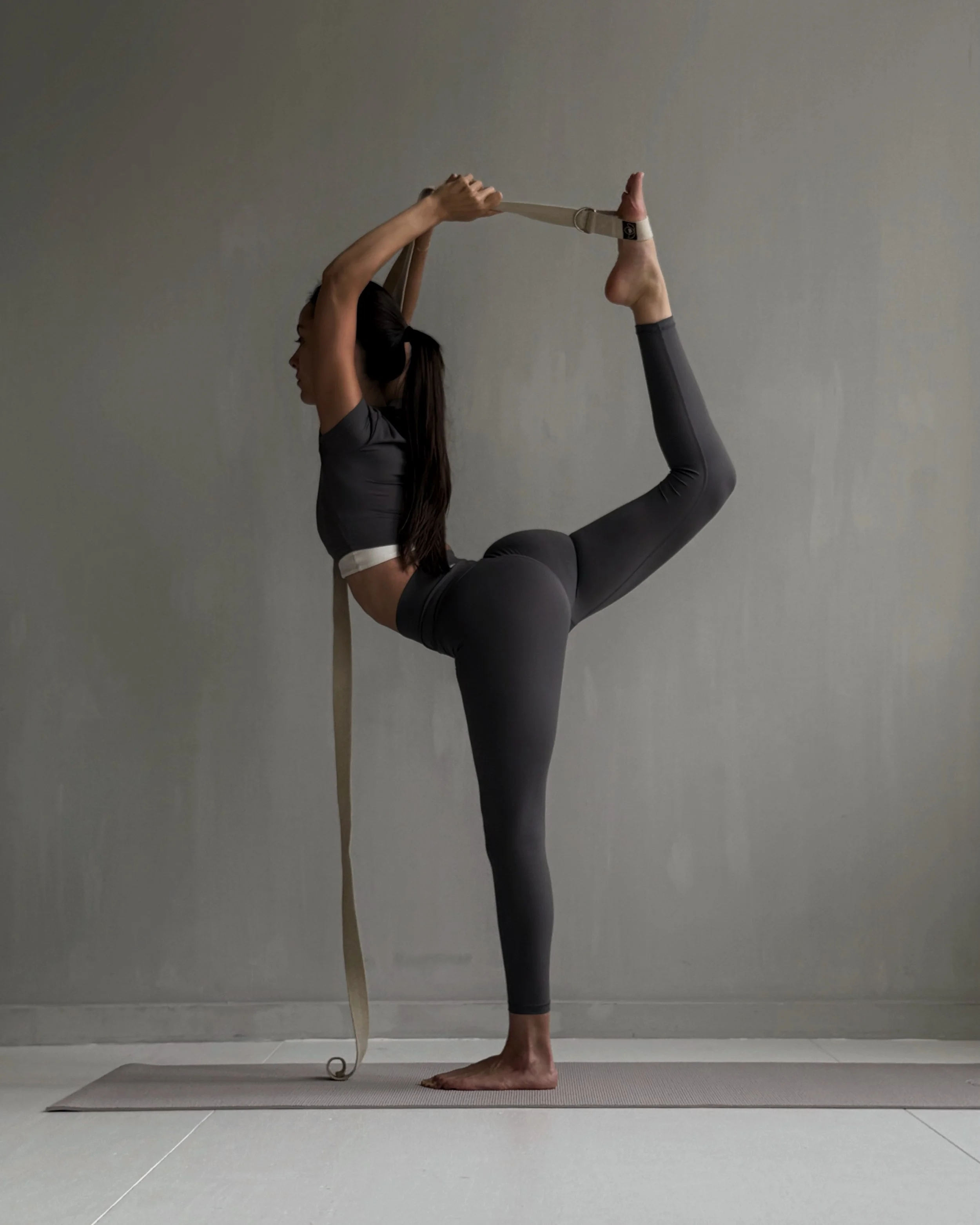 Woman performing a yoga pose with a stretching strap on a yoga mat.