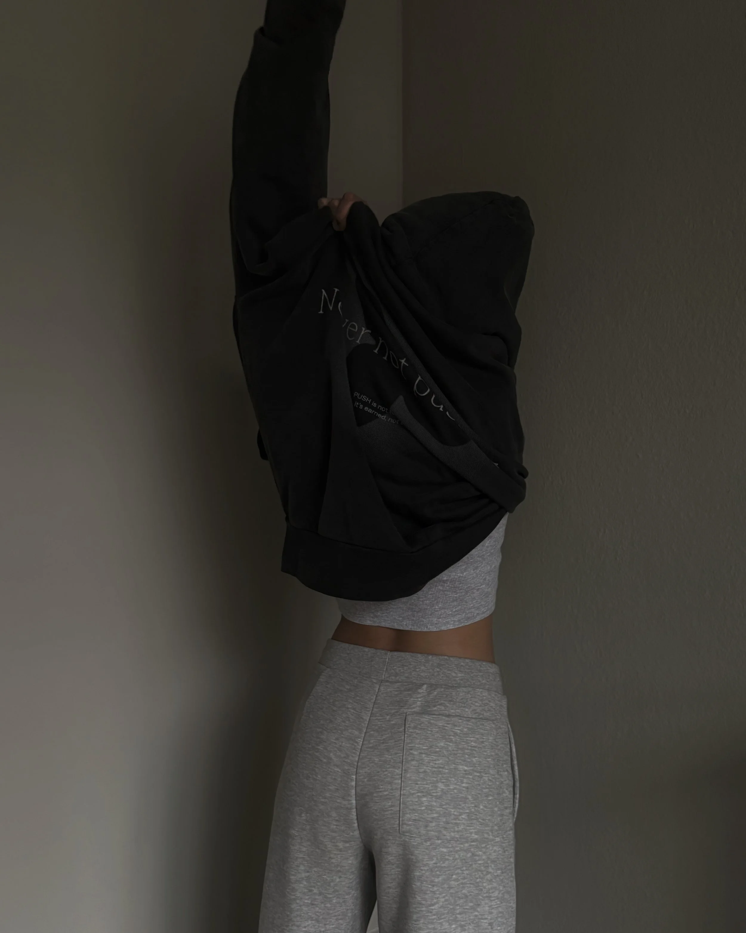 Creator pulling on a black hoodie over a grey lounge set.