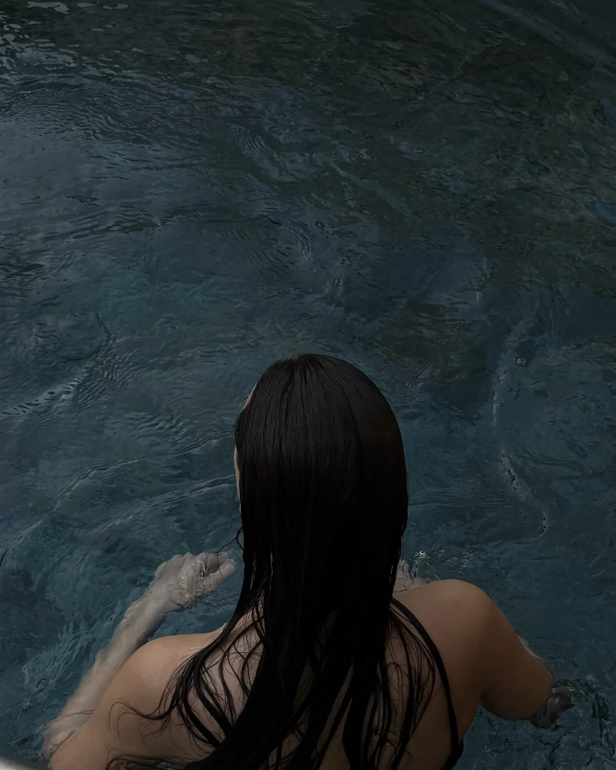 Woman relaxing in an outdoor pool with her back to the camera.