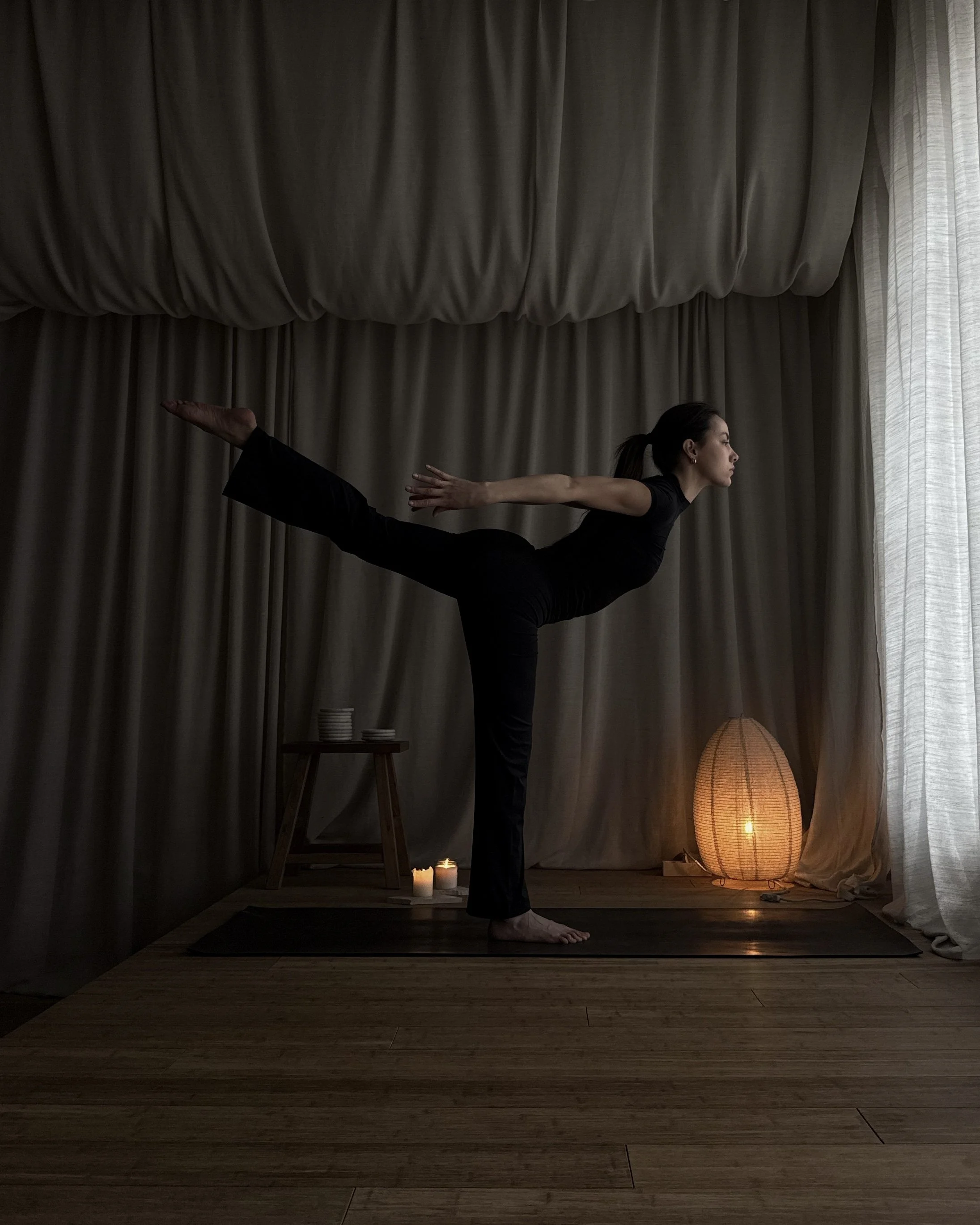 Woman balancing in a standing yoga pose in a softly lit studio.