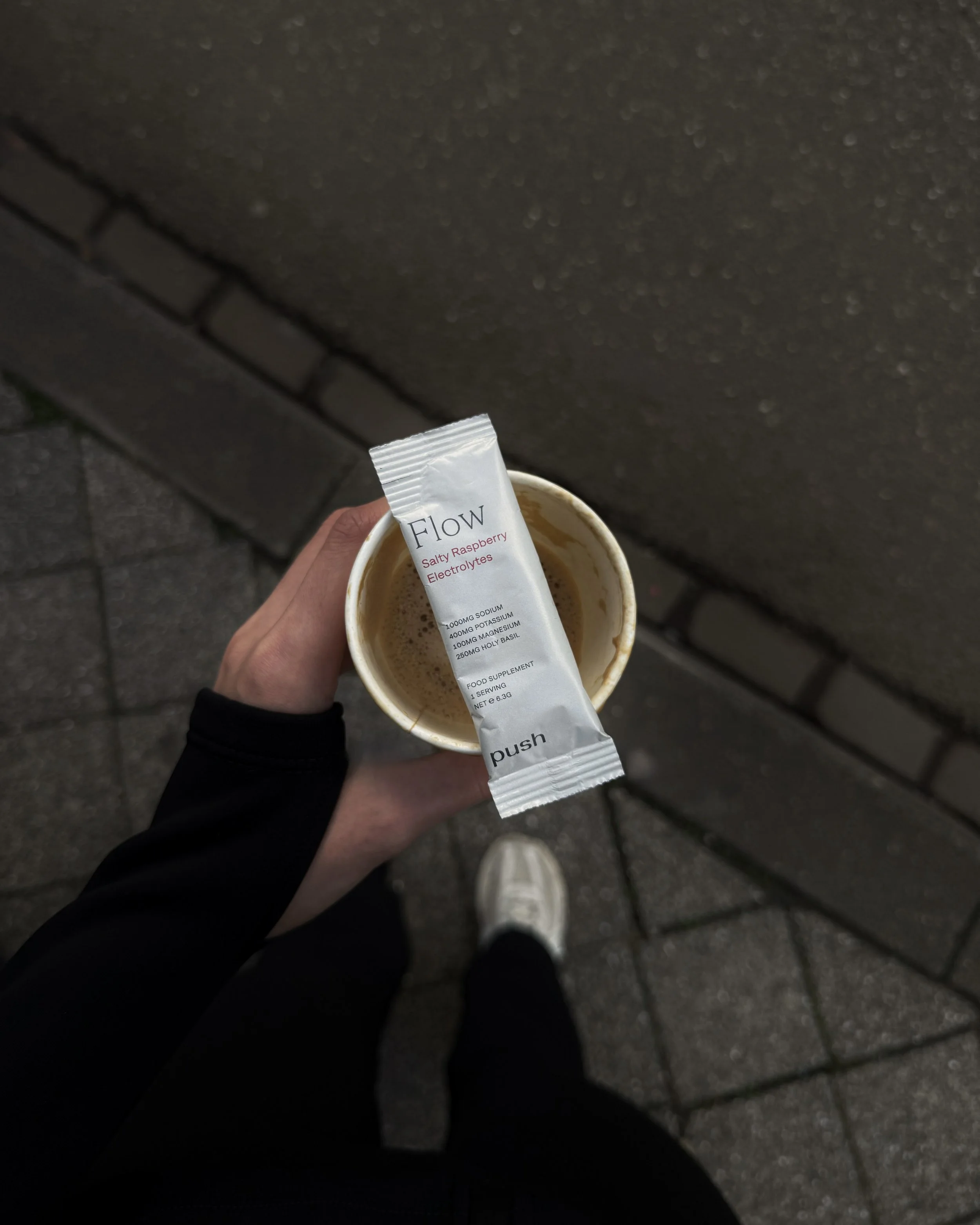 Hand holding a coffee and electrolyte sachet while walking outdoors.