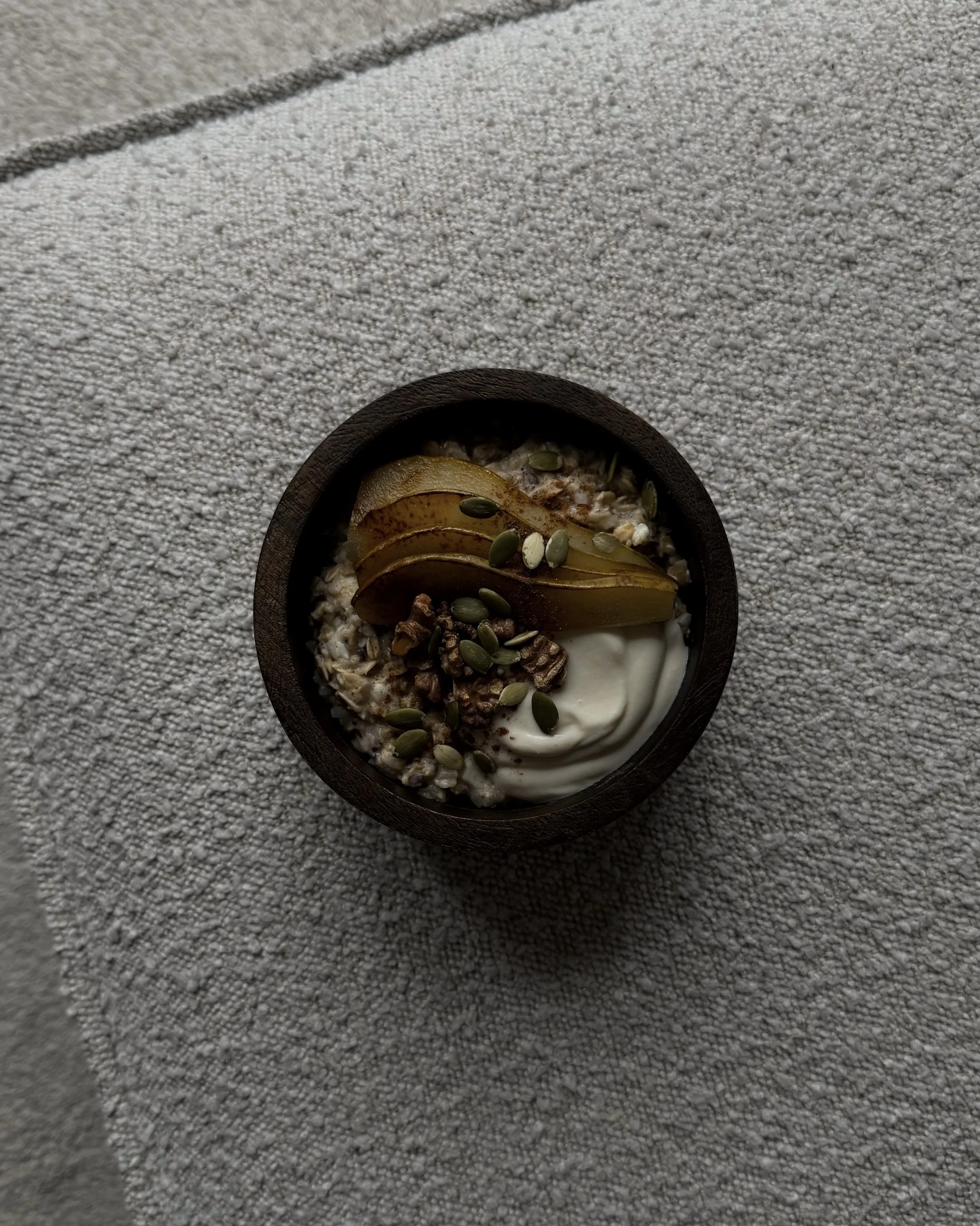 Bowl of oatmeal topped with poached pear, yogurt, walnuts and pumpkin seeds.