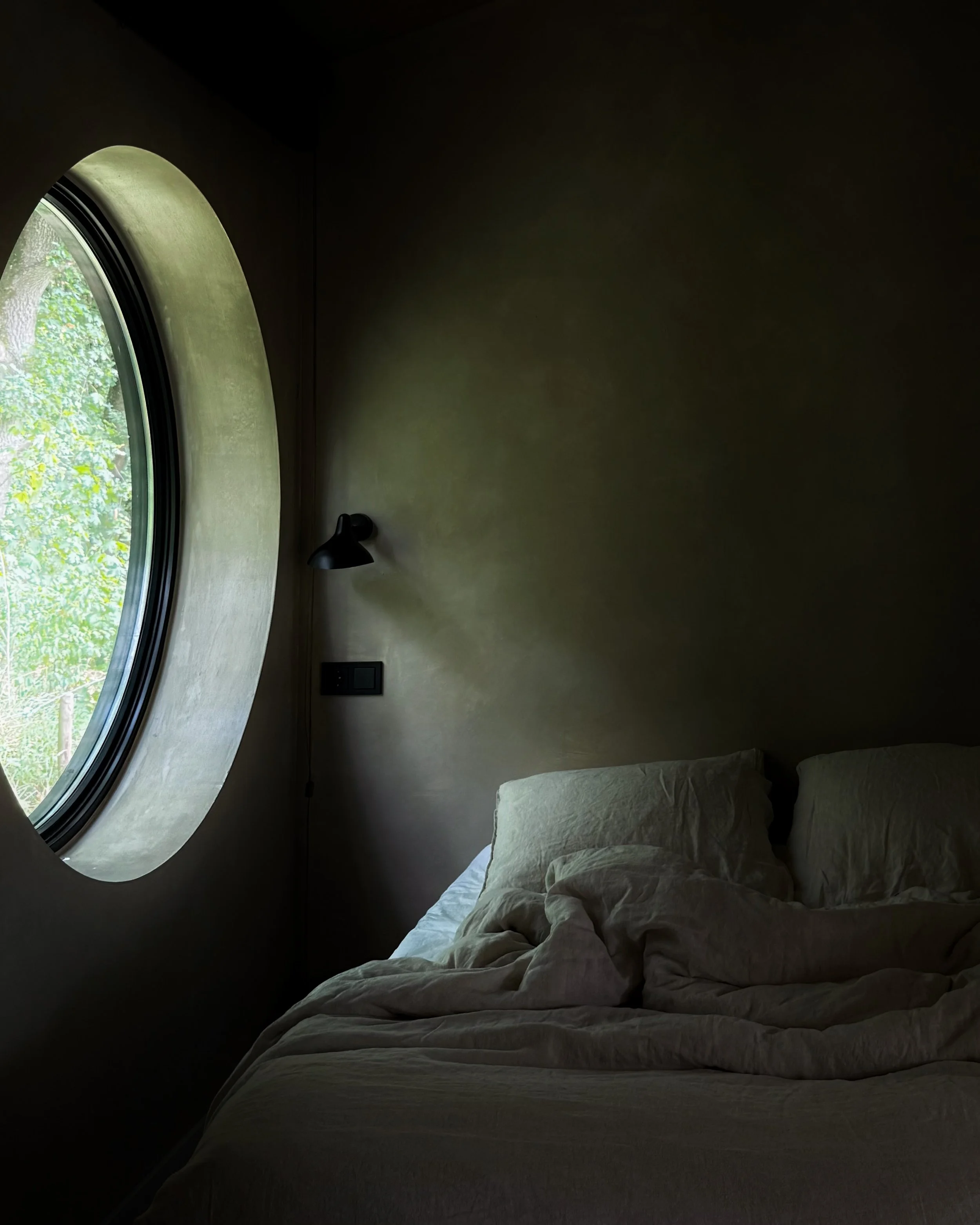 Minimalist bedroom with white bedding and a round window.