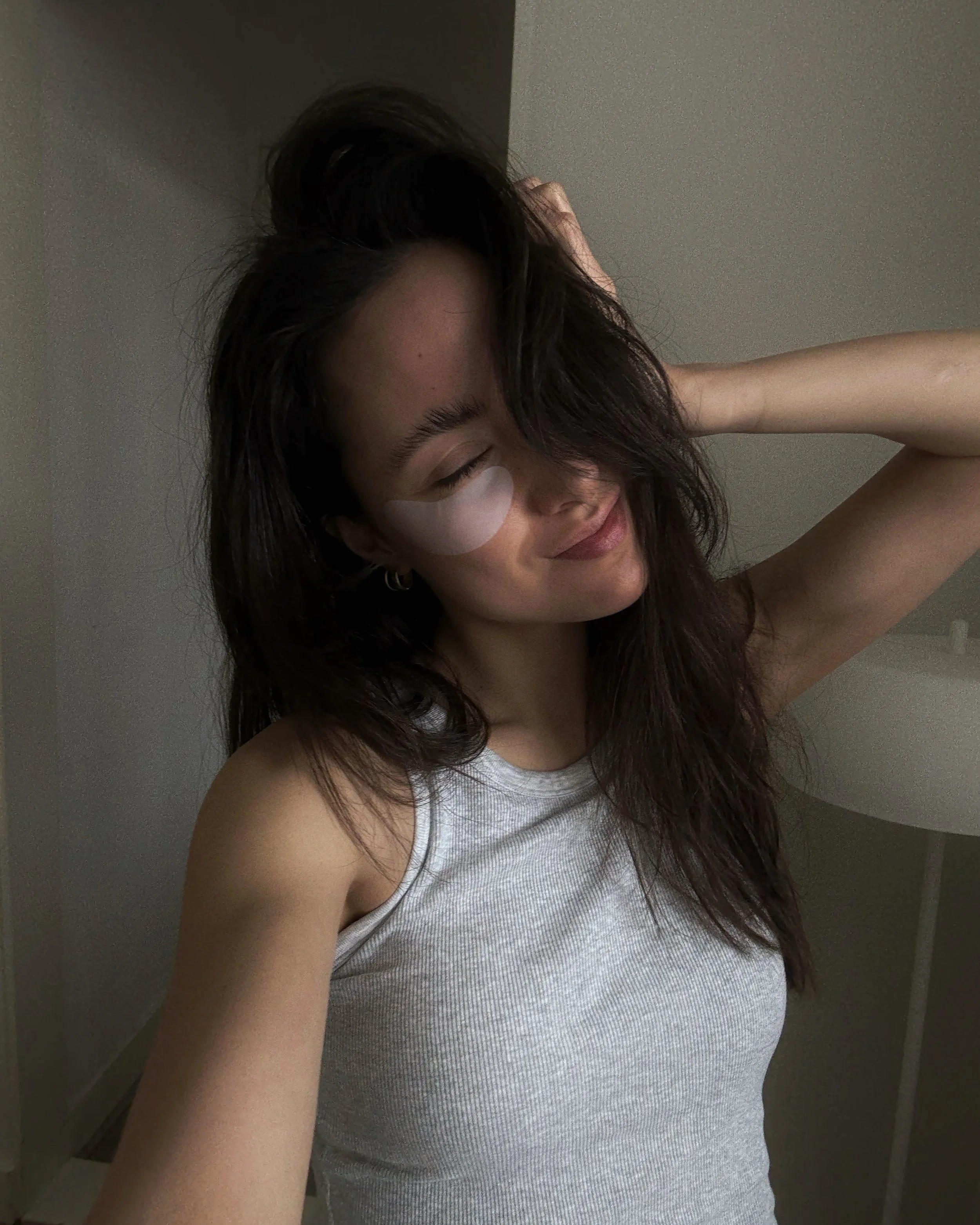 Woman smiling with under-eye patches during a morning skincare routine.