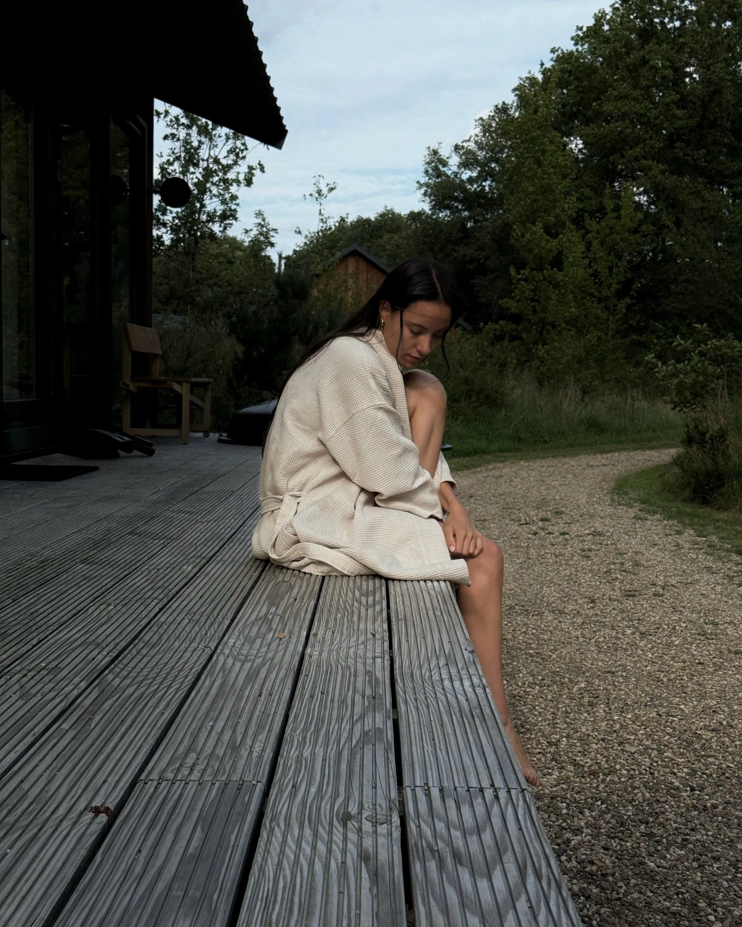 Creator sitting on a wooden deck in a cream robe surrounded by nature.