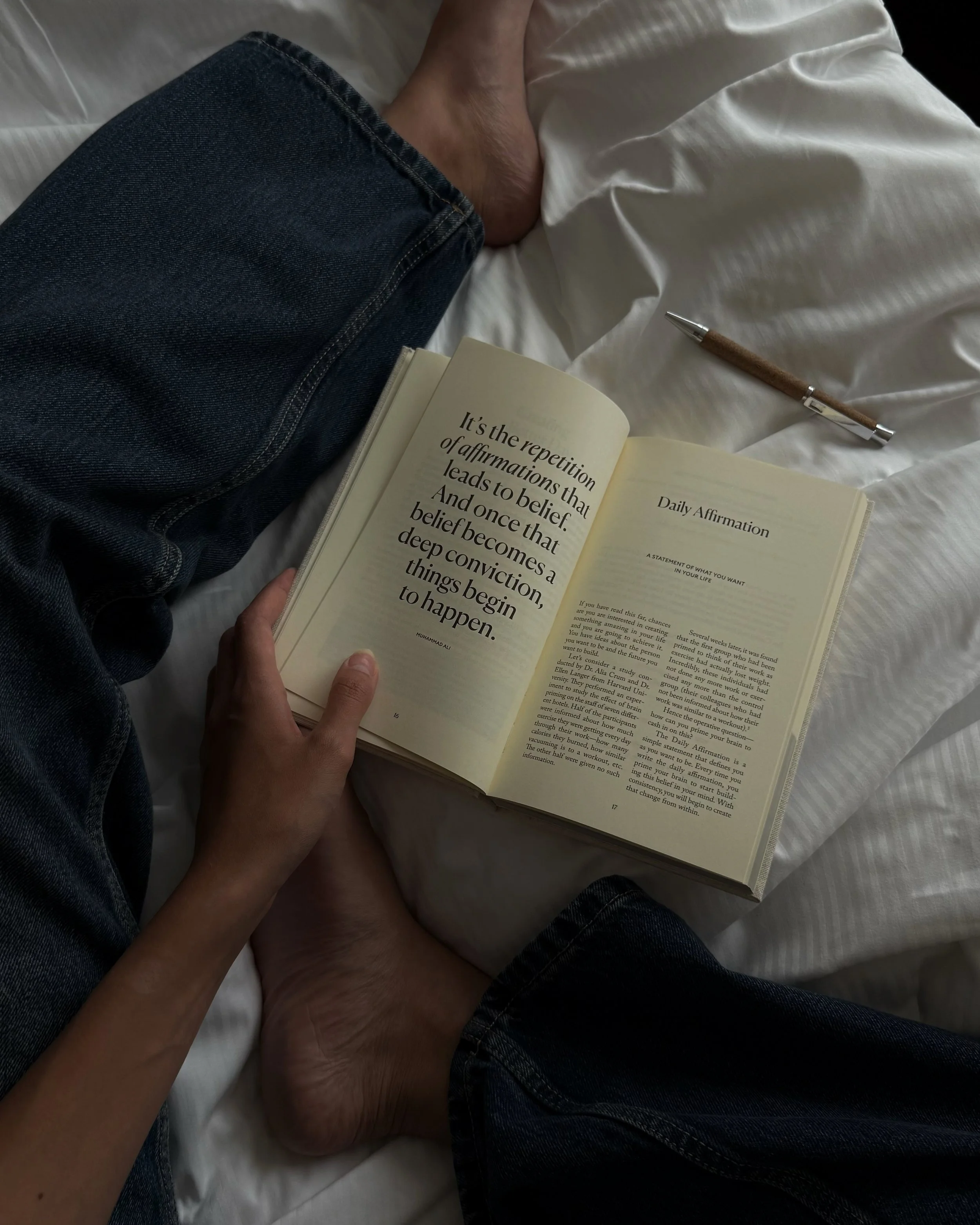 Reading a personal growth book in bed with a notebook nearby.
