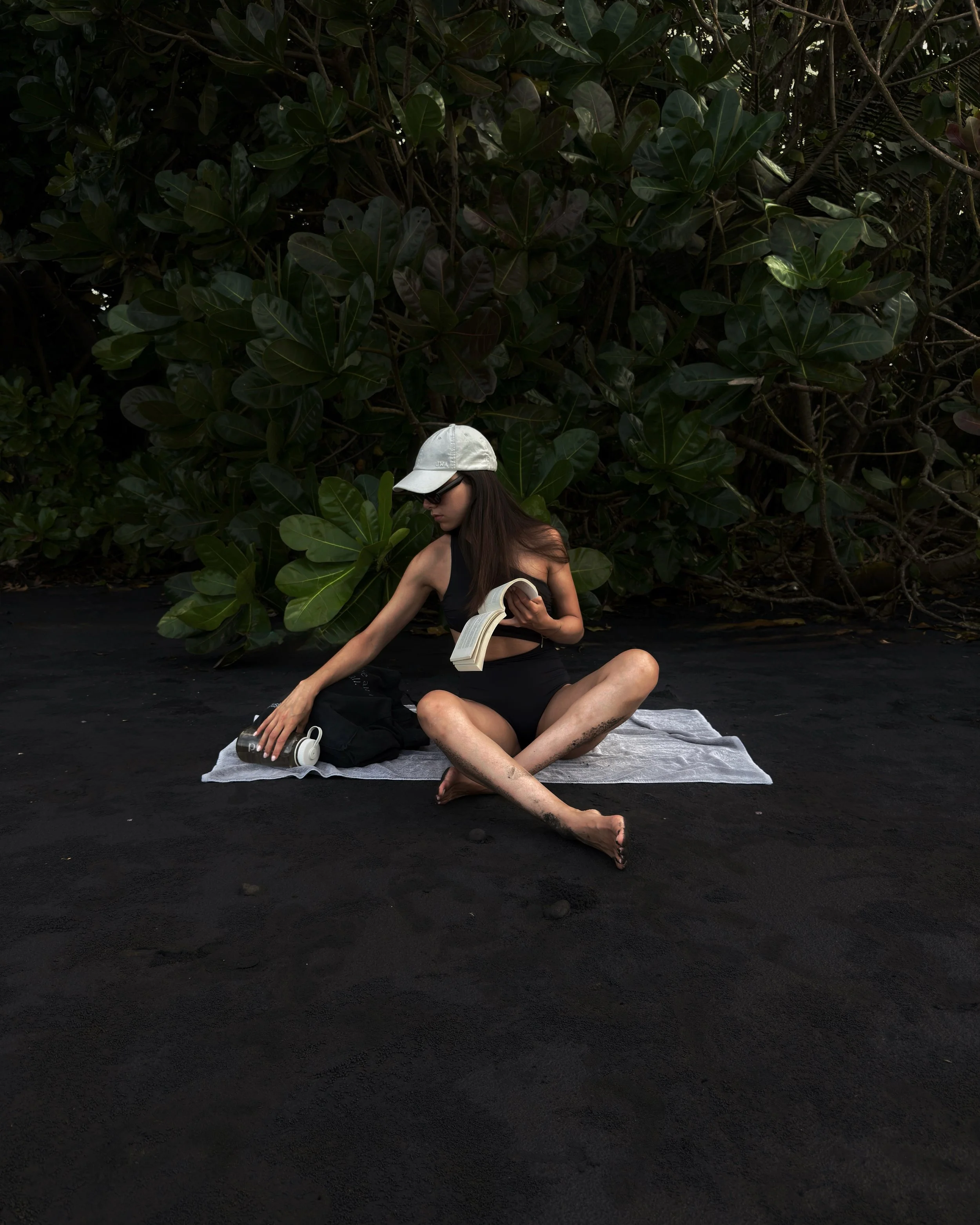 Creator relaxing on a black sand beach with a book and beach essentials.
