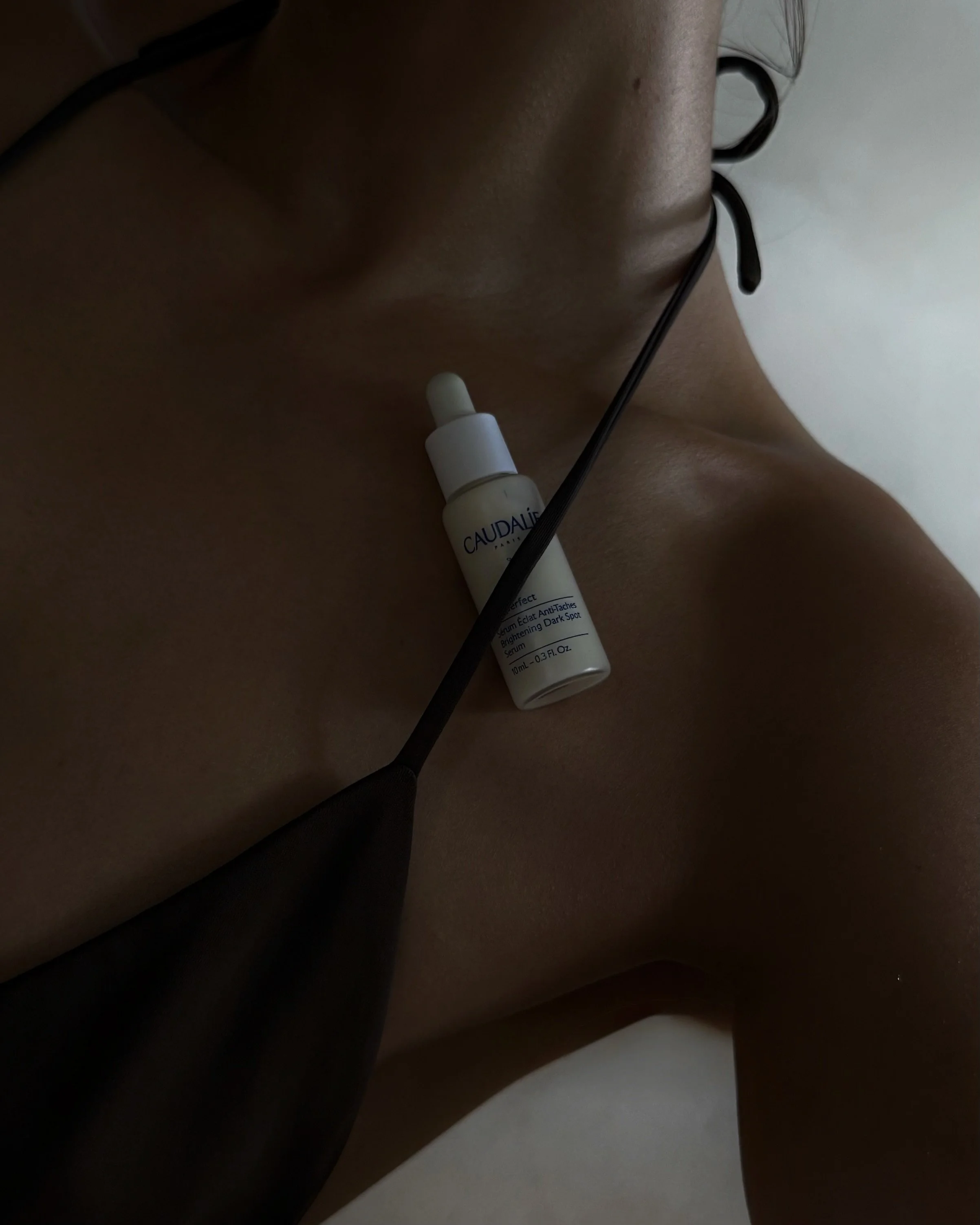Close-up of a skincare serum bottle resting on the shoulder.