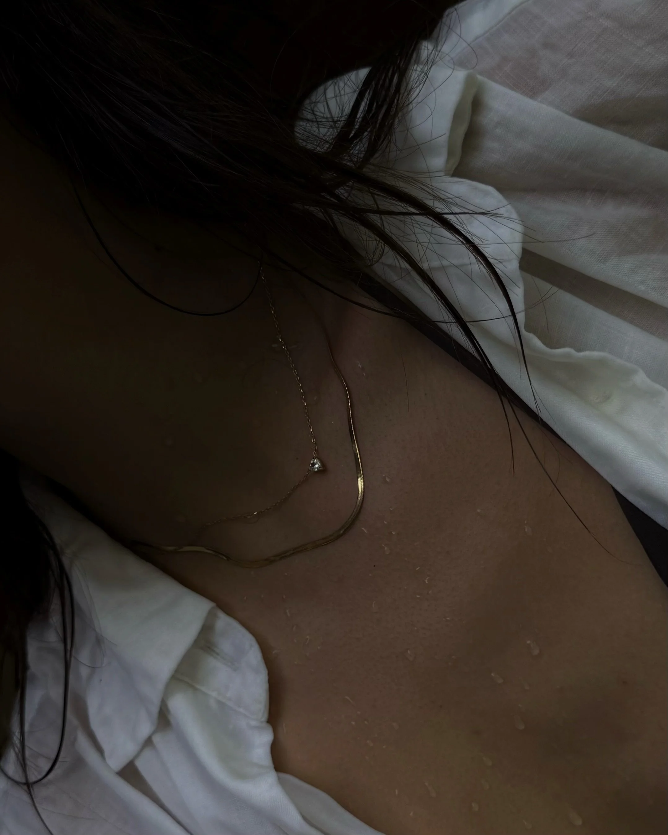 Close-up of a gold necklace resting on wet skin.