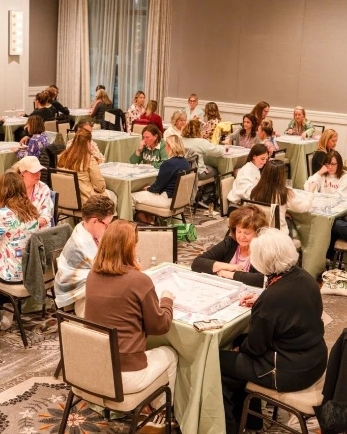 A large room filled with women sitting at tables playing American Mahjong.