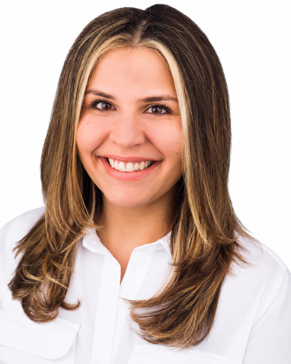 A woman with shoulder-length brown hair with blonde highlights, smiling broadly, wearing a white blouse, against a white background.