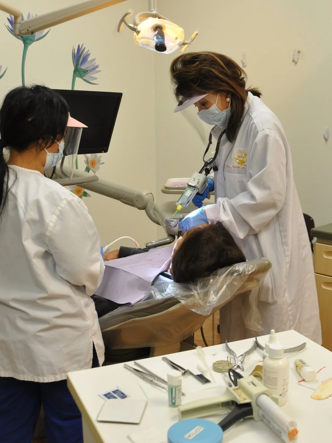 Medical professionals in scrubs and masks performing a dental procedure on a patient in a clinic with dental tools and equipment.