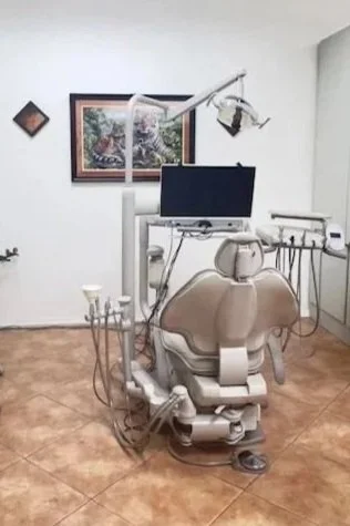 A dental clinic treatment room with a dental chair, overhead light, monitor, and dental equipment.