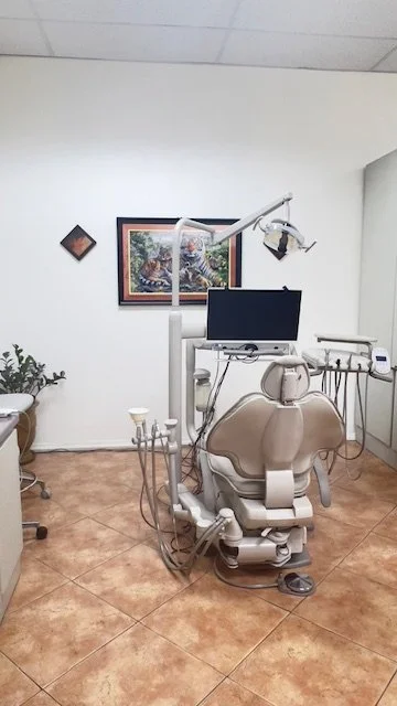 Empty dental examination room with dental chair, monitor, and equipment, with framed artwork on the wall.