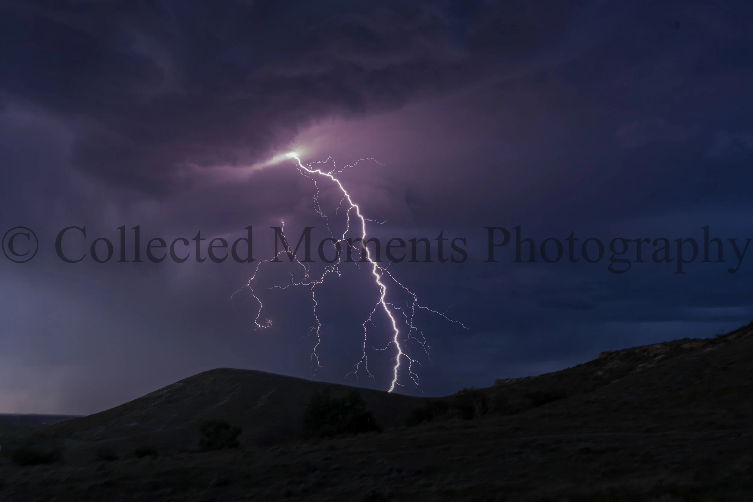Lightning strikes during a dark thunderstorm over a hill or mountain landscape at night.