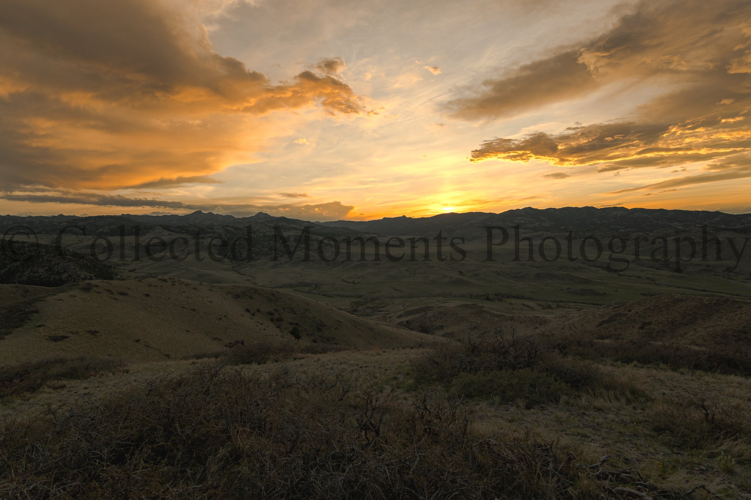 Sunset over rolling hills with scattered clouds in the sky.