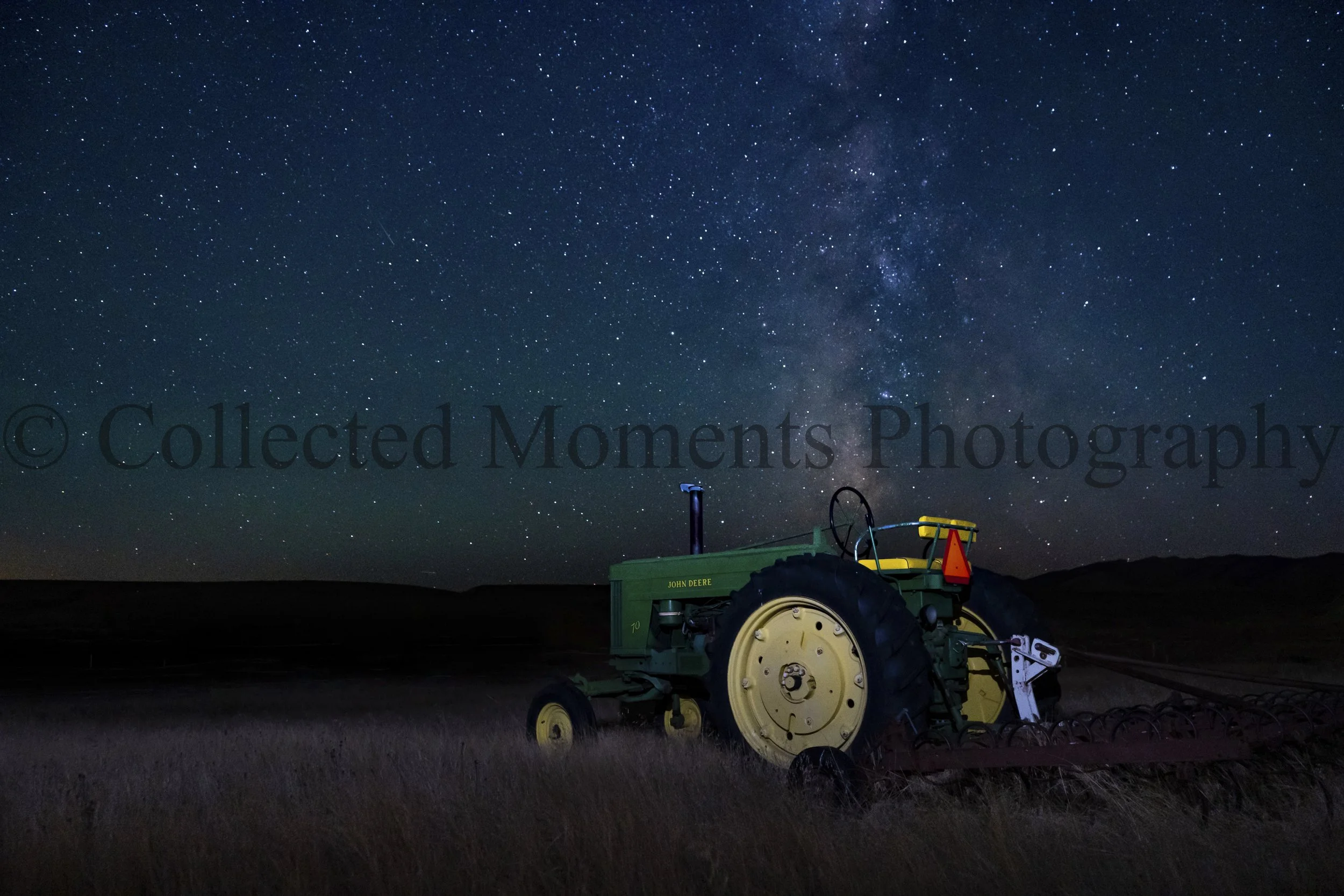 Night sky filled with numerous stars and the Milky Way galaxy, with a John Deere tractor and farming equipment in the foreground.