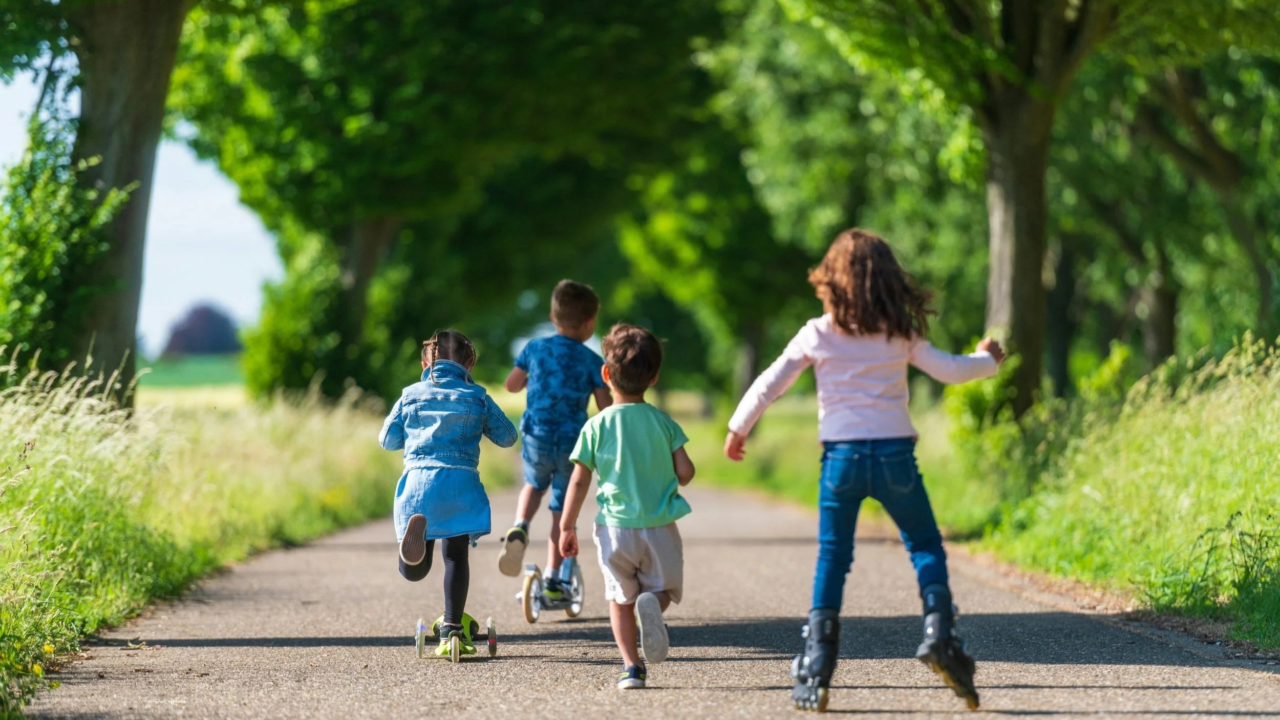 Children running and playing outdoors on a sunny day, with greenery and trees in the background.