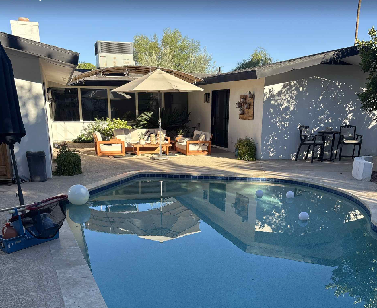 Backyard with a swimming pool, outdoor seating area with chairs and cushions, and lush greenery.