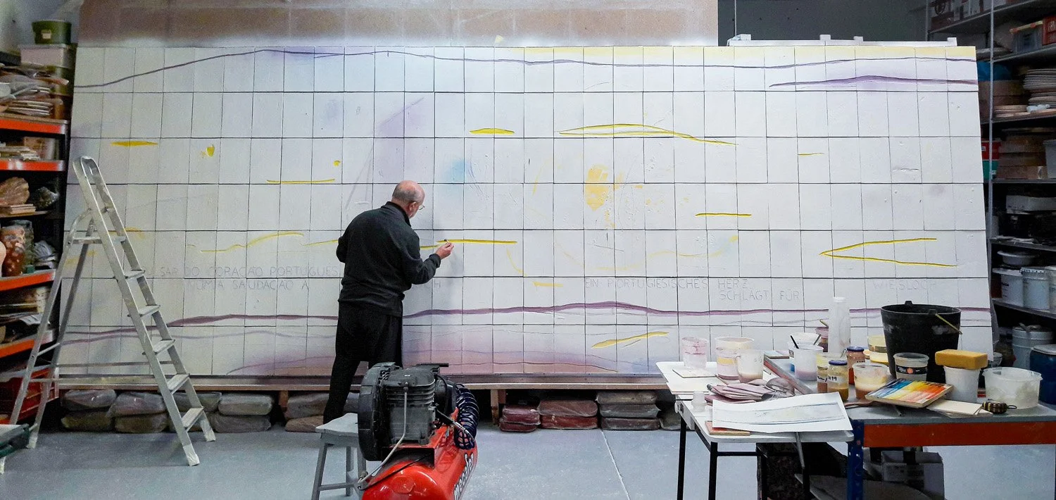 Francisco Laranjo painting a mural on a large wall in an art studio, surrounded by art supplies and a ladder.