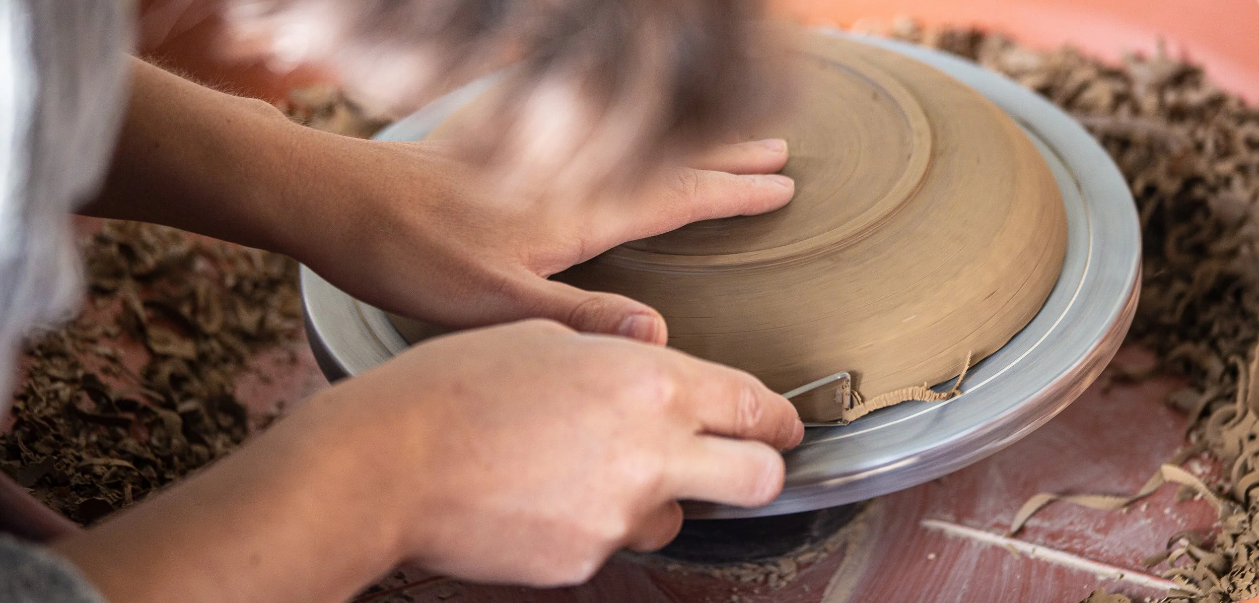 Person shaping clay on a pottery wheel with dried leaves scattered around.