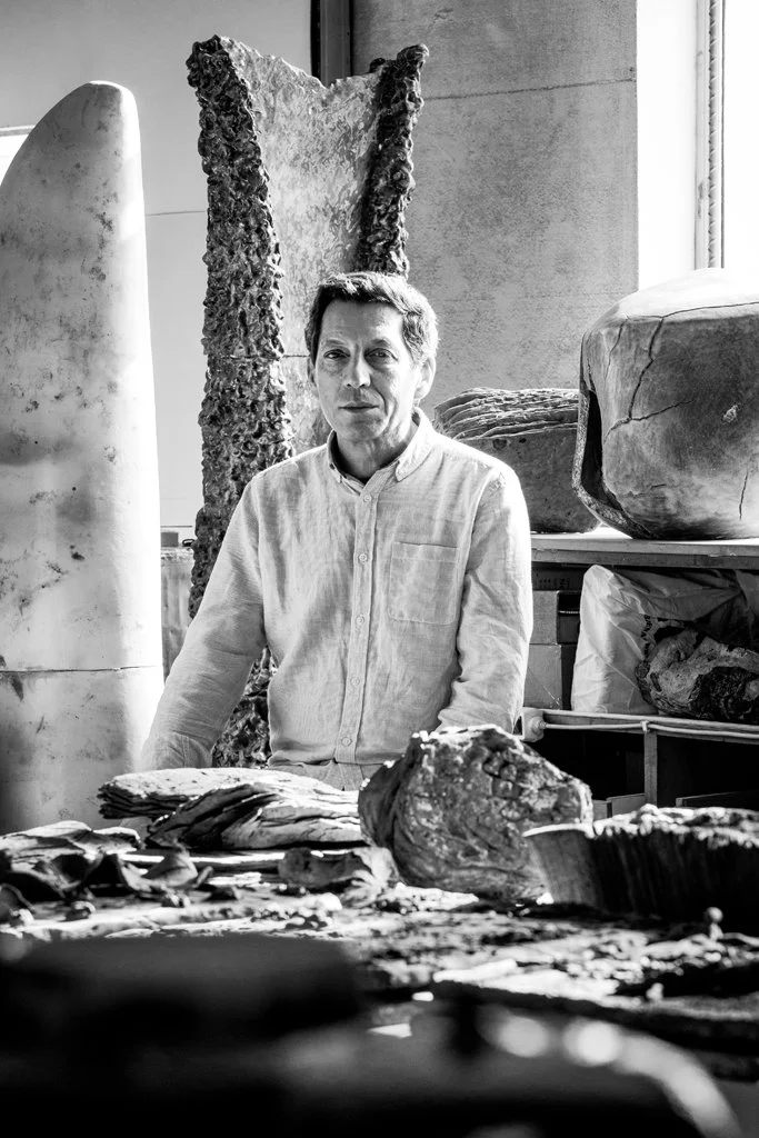 João Carqueijeiro inside his studio surrounded by large sculptures and artifacts, looking towards the camera.