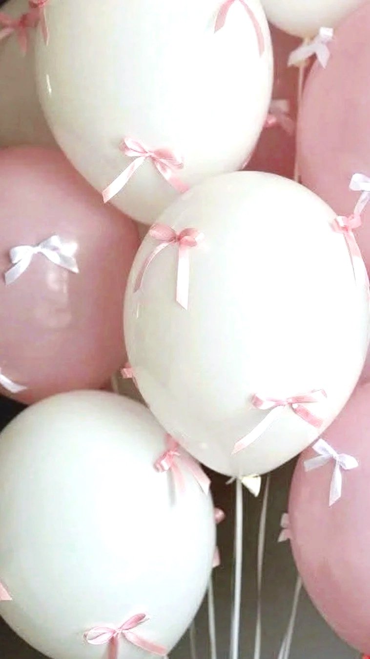 A bunch of white and pink balloons decorated with small satin ribbons tied in bows.