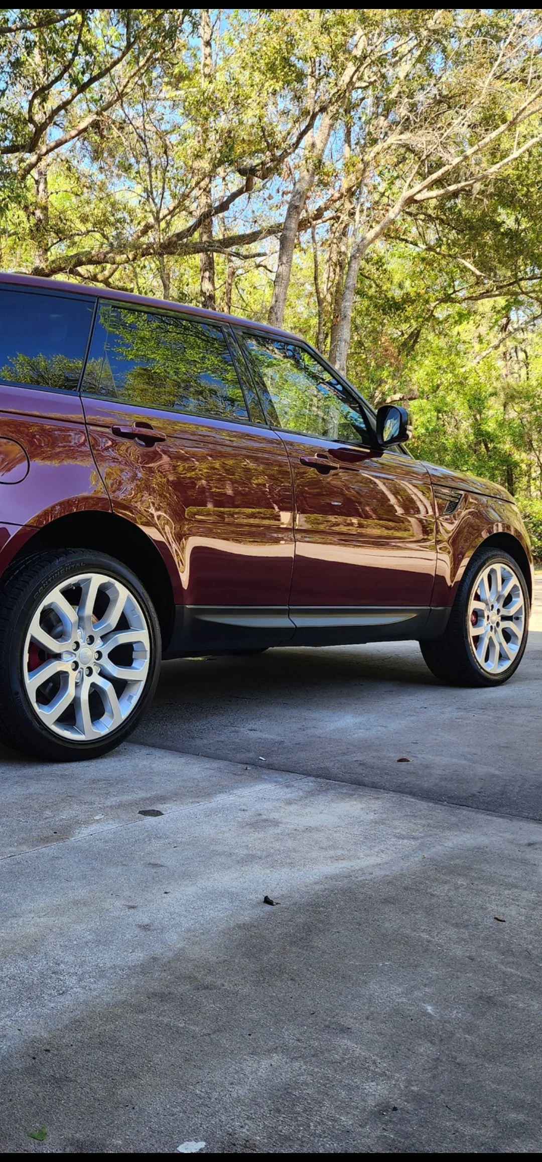 A maroon-colored SUV parked on a concrete driveway with green trees and a blue sky reflected in its windows.