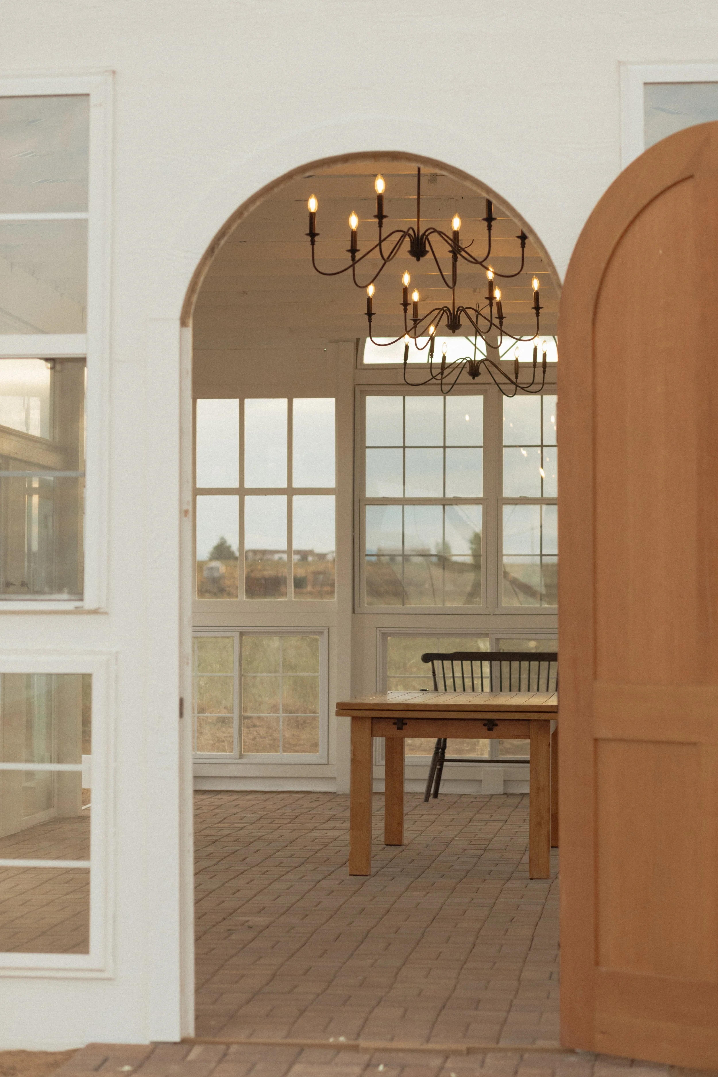 Interior view of a room with large windows, a wooden table, a modern metal chair, and a chandelier hanging from the ceiling.