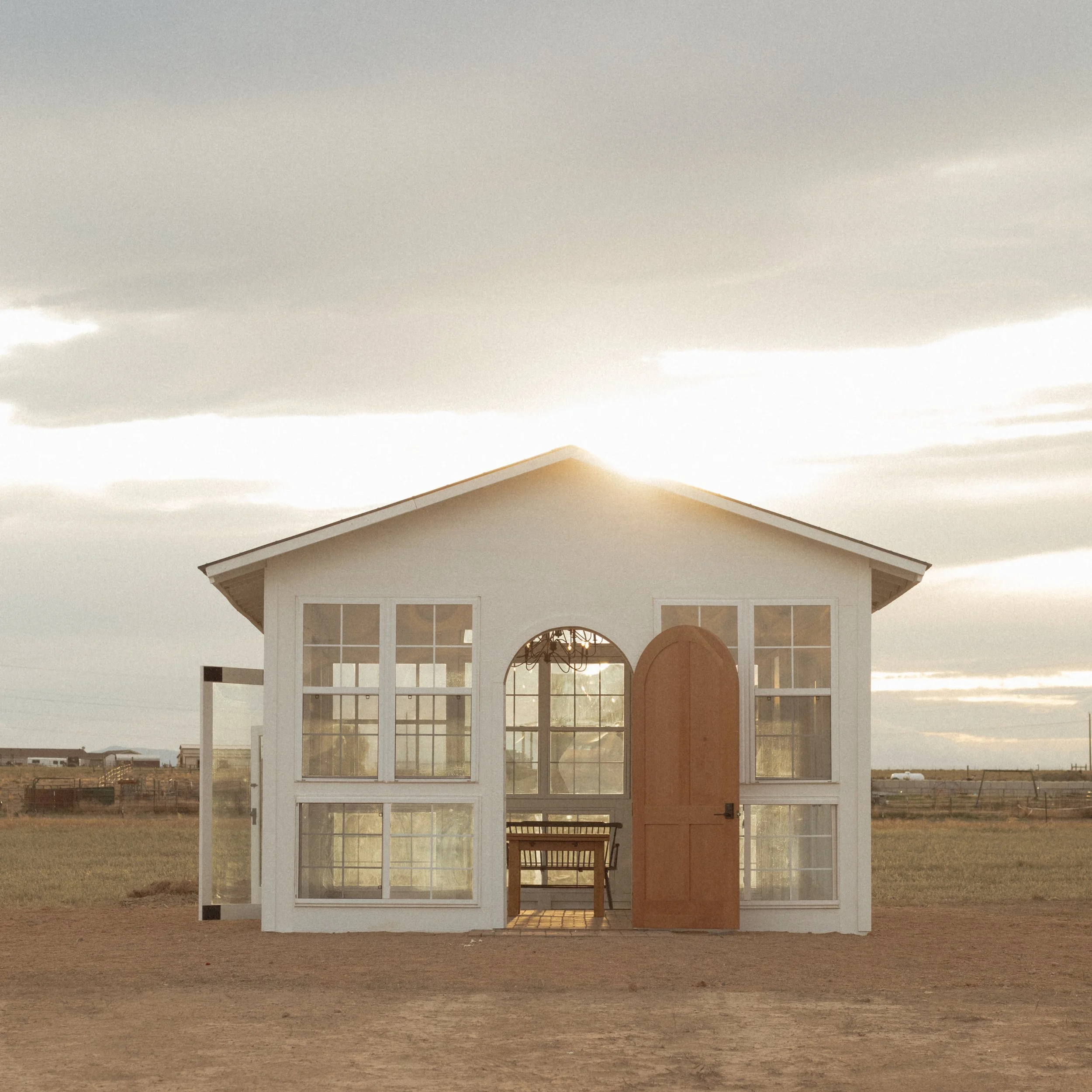 A house with a large porch, situated in the middle of an open field with clear skies and some clouds.