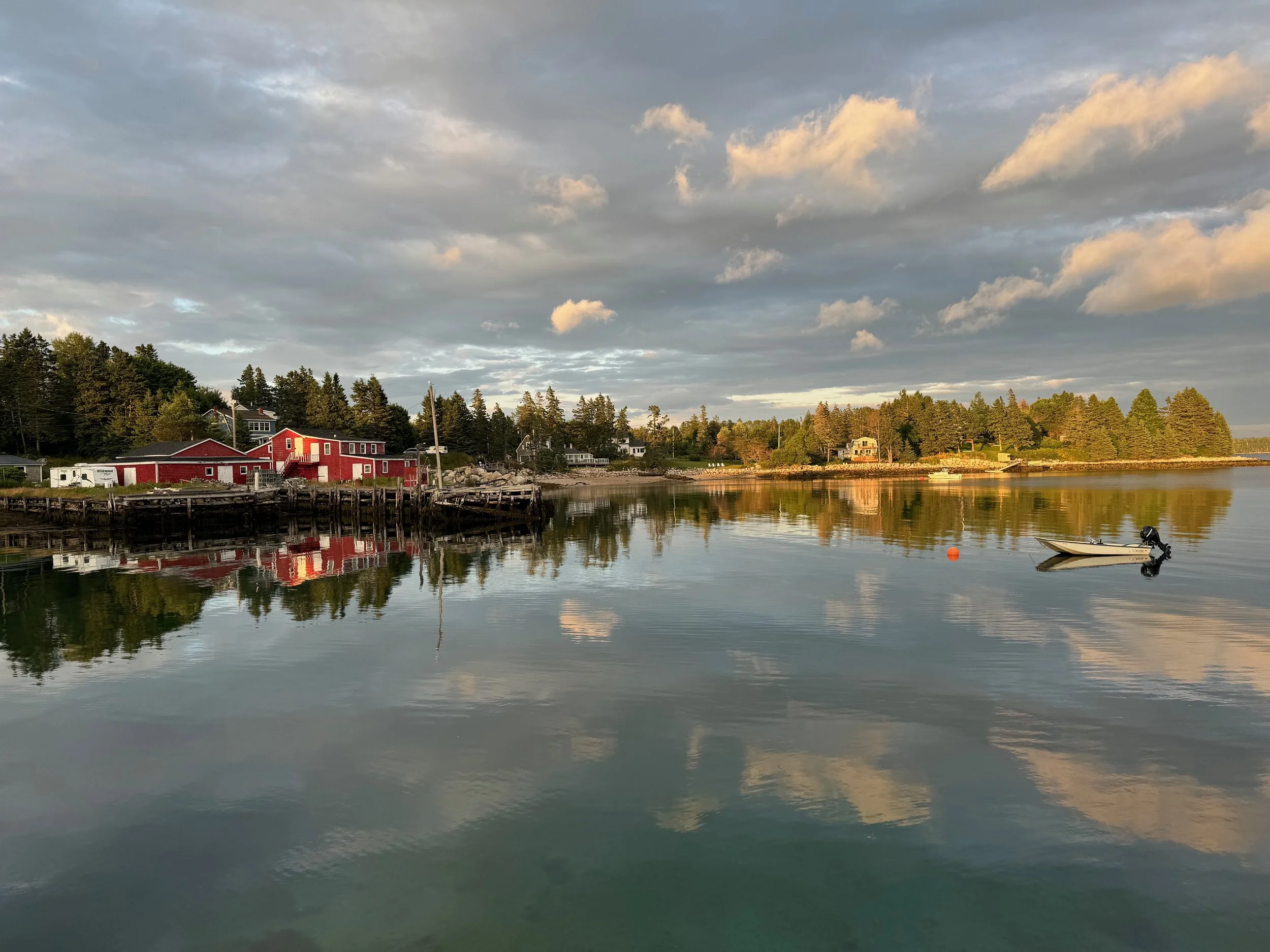 Calm water reflecting a cloudy sky with a few small houses and trees along the shoreline.
