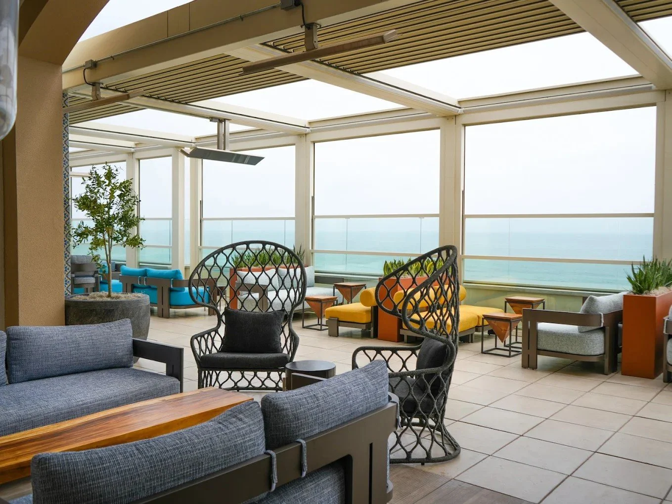Spacious rooftop lounge with woven signature chairs, modern furniture, and a retractable louver roof overlooking the ocean.