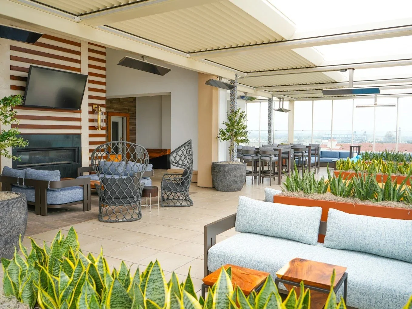 Contemporary rooftop lounge with a striped fireplace wall, retractable roof, and coastal views through tall glass enclosures.
