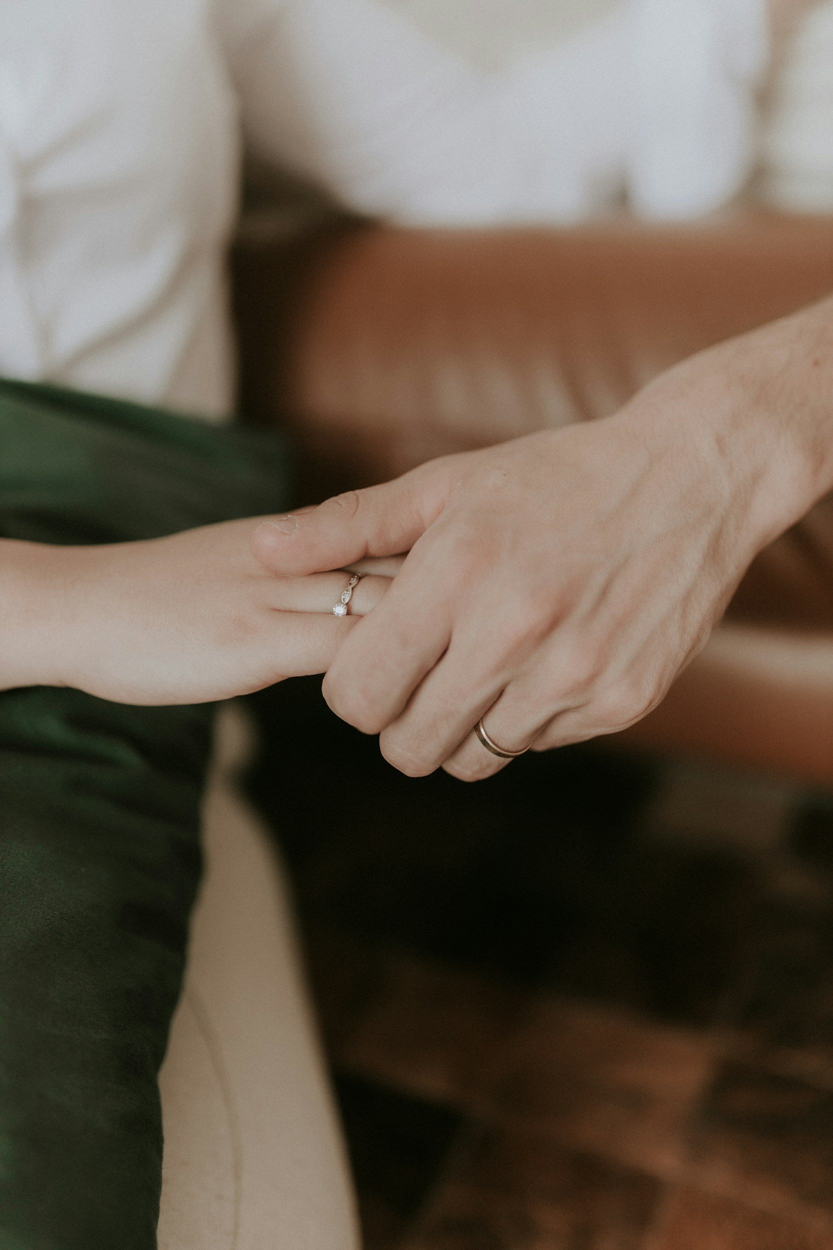 A close-up of two people holding hands, with wedding rings visible on their fingers.