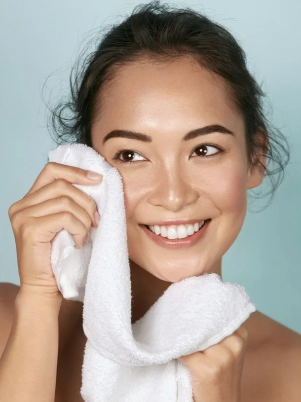 A young woman smiling and wiping her face with a white towel.