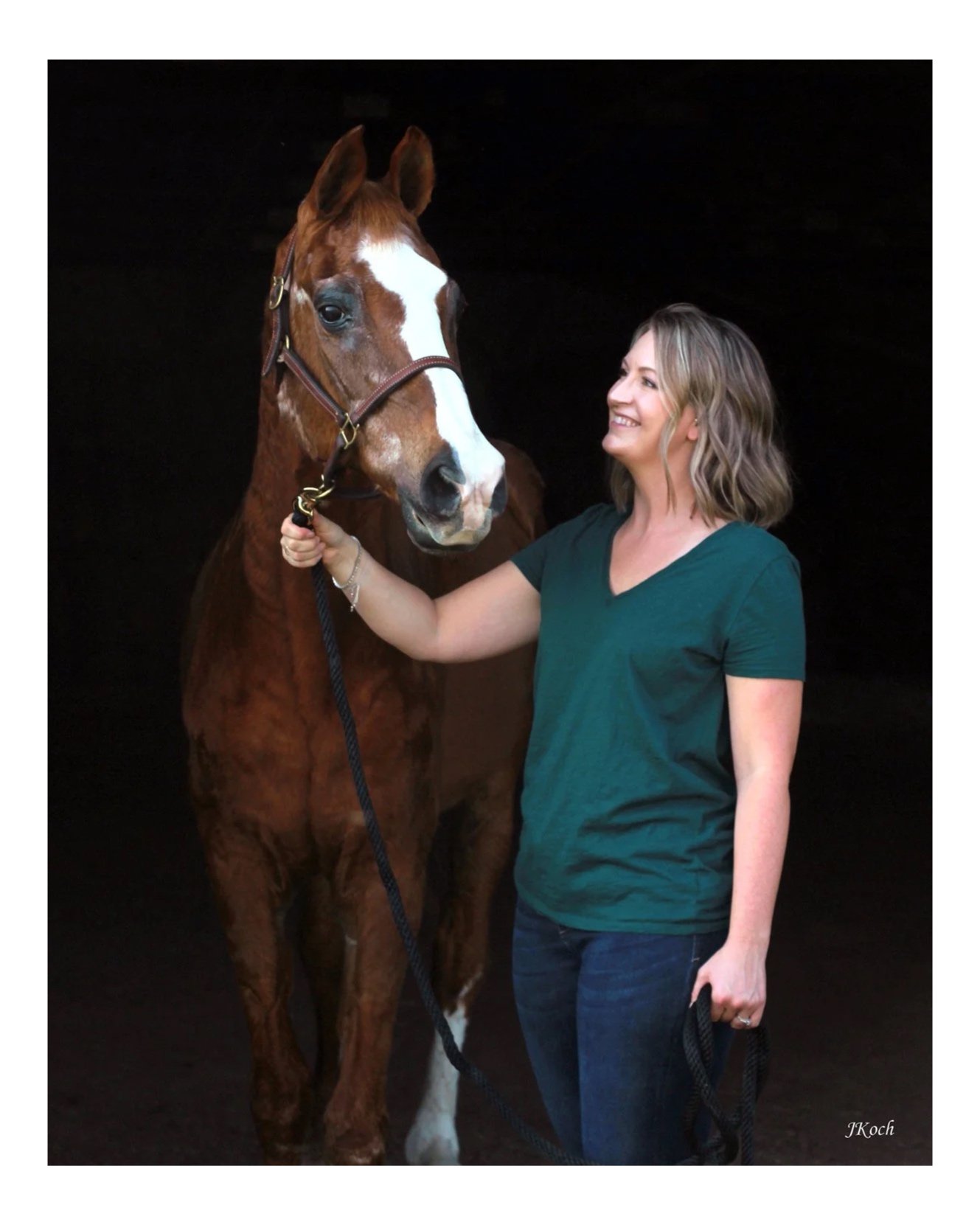 A woman smiling and holding a red and white horse by the bridle, against a dark background.