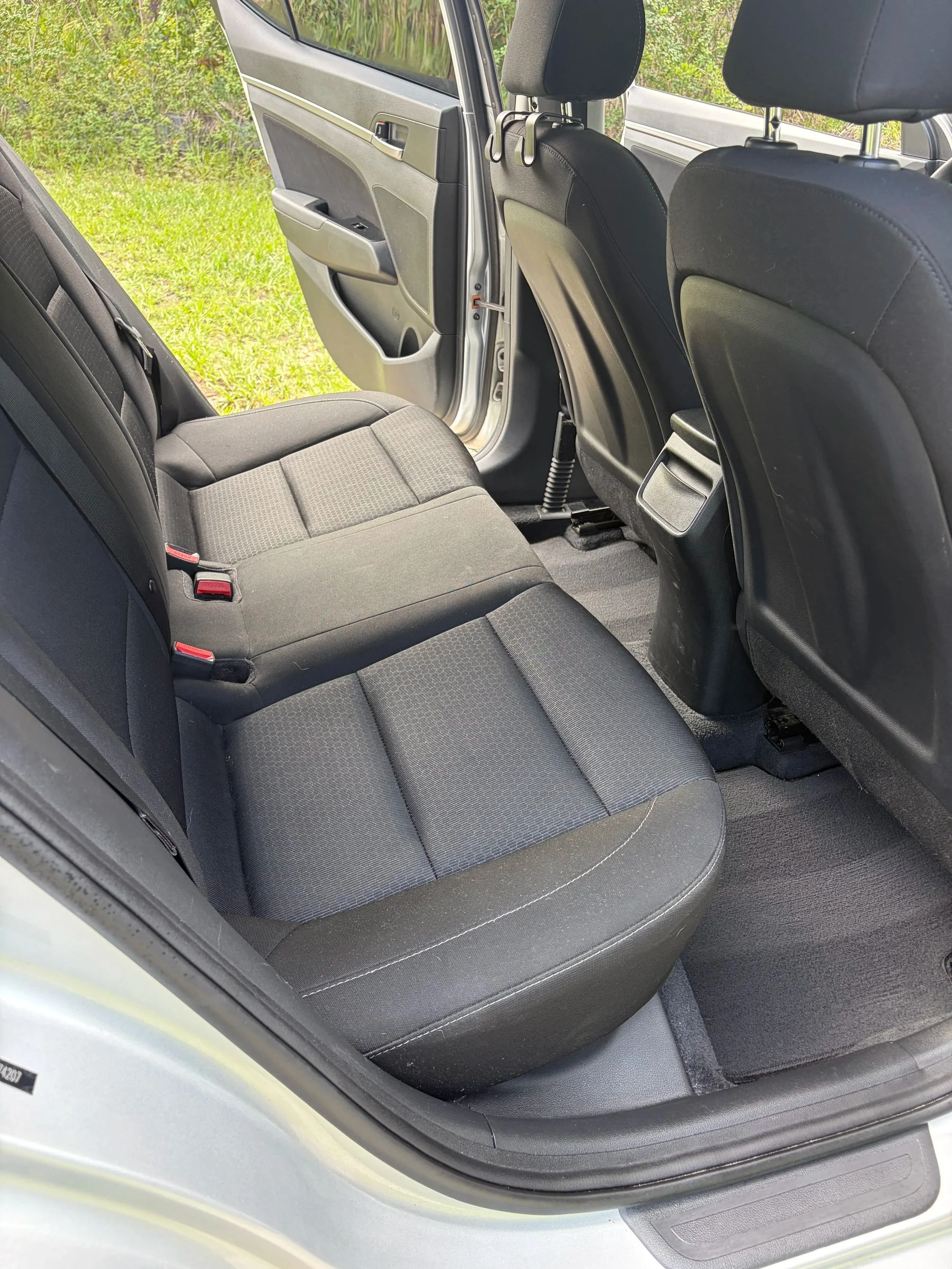 Rear passenger area after professional interior detailing with clean black cloth seats, vacuumed carpet, and restored interior.