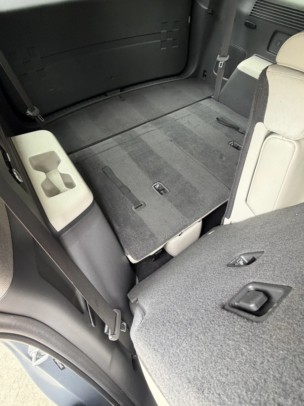 The interior of a vehicle with the back seats folded down to create a flat cargo area, with carpeting and latches visible.