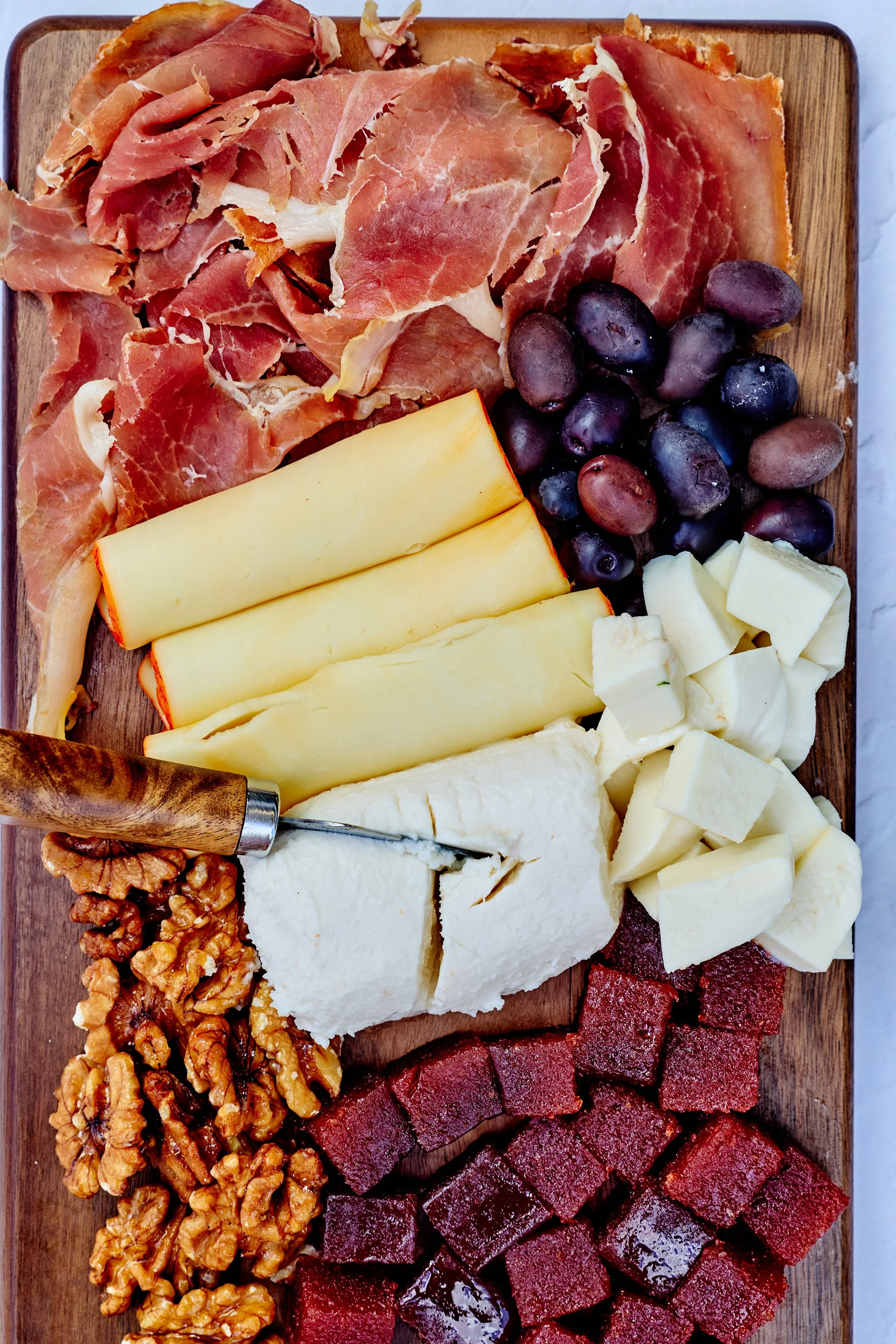A cheese and charcuterie board with various meats, cheeses, grapes, and nuts on a wooden platter.
