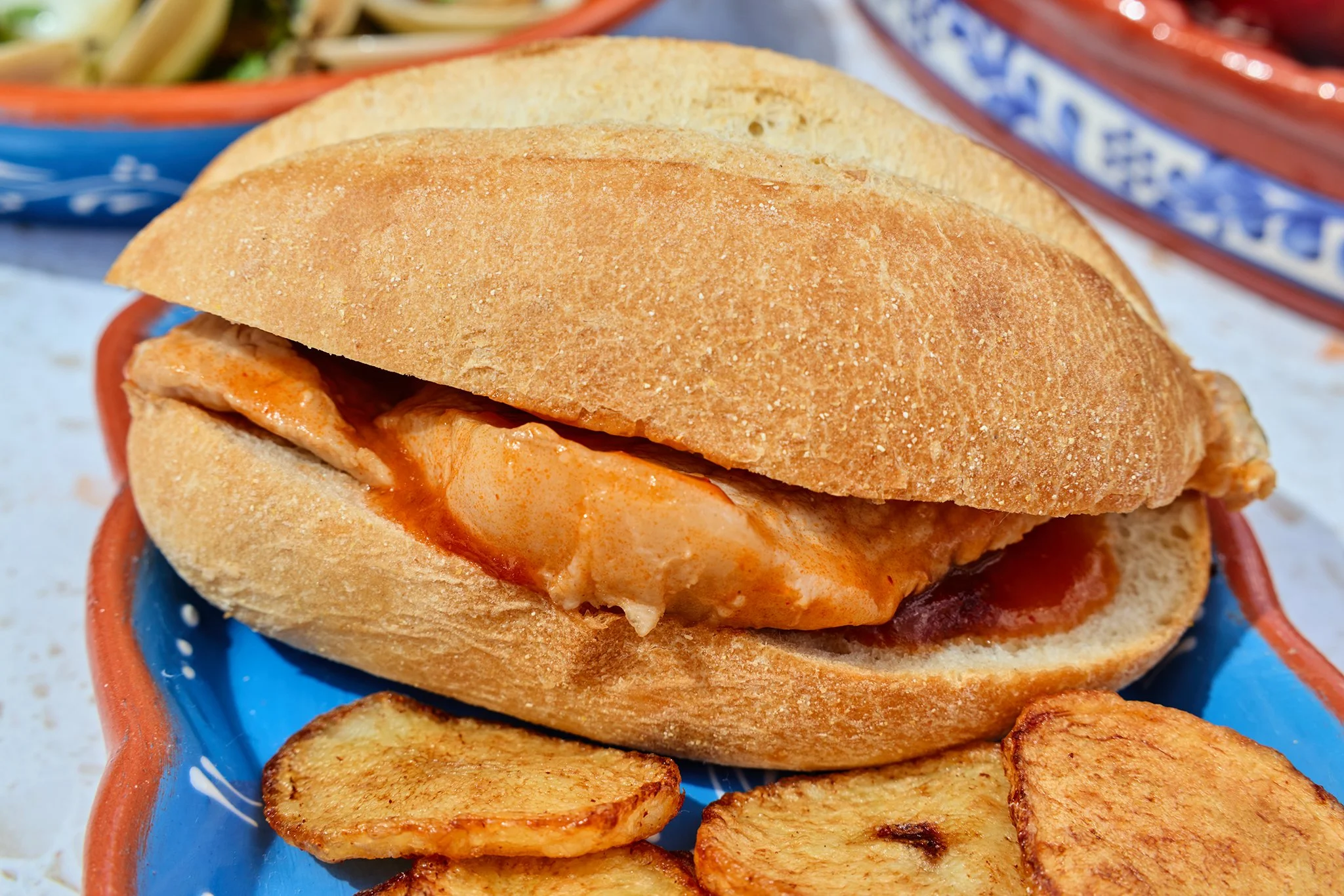 A close-up of a Portuguese sandwich with fried potato slices in a blue dish.