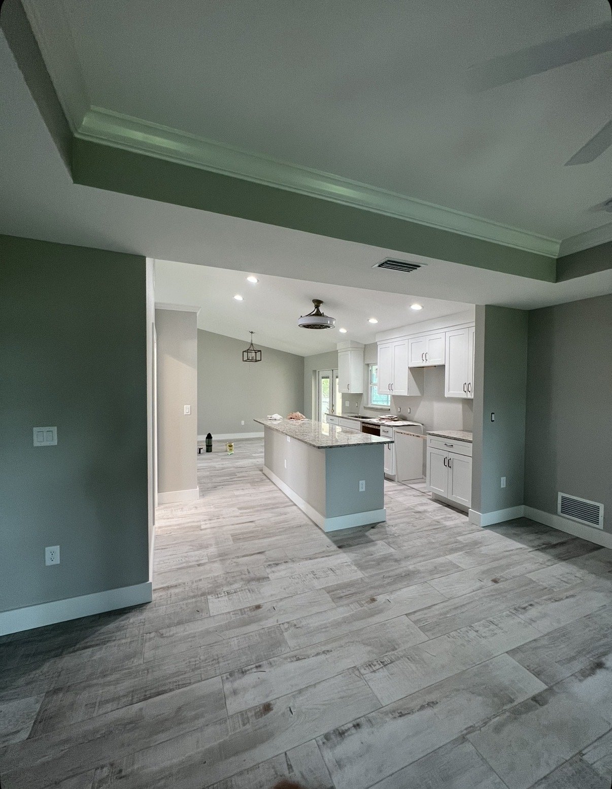 Empty kitchen with white cabinets, granite countertops, and light-colored wood flooring.
