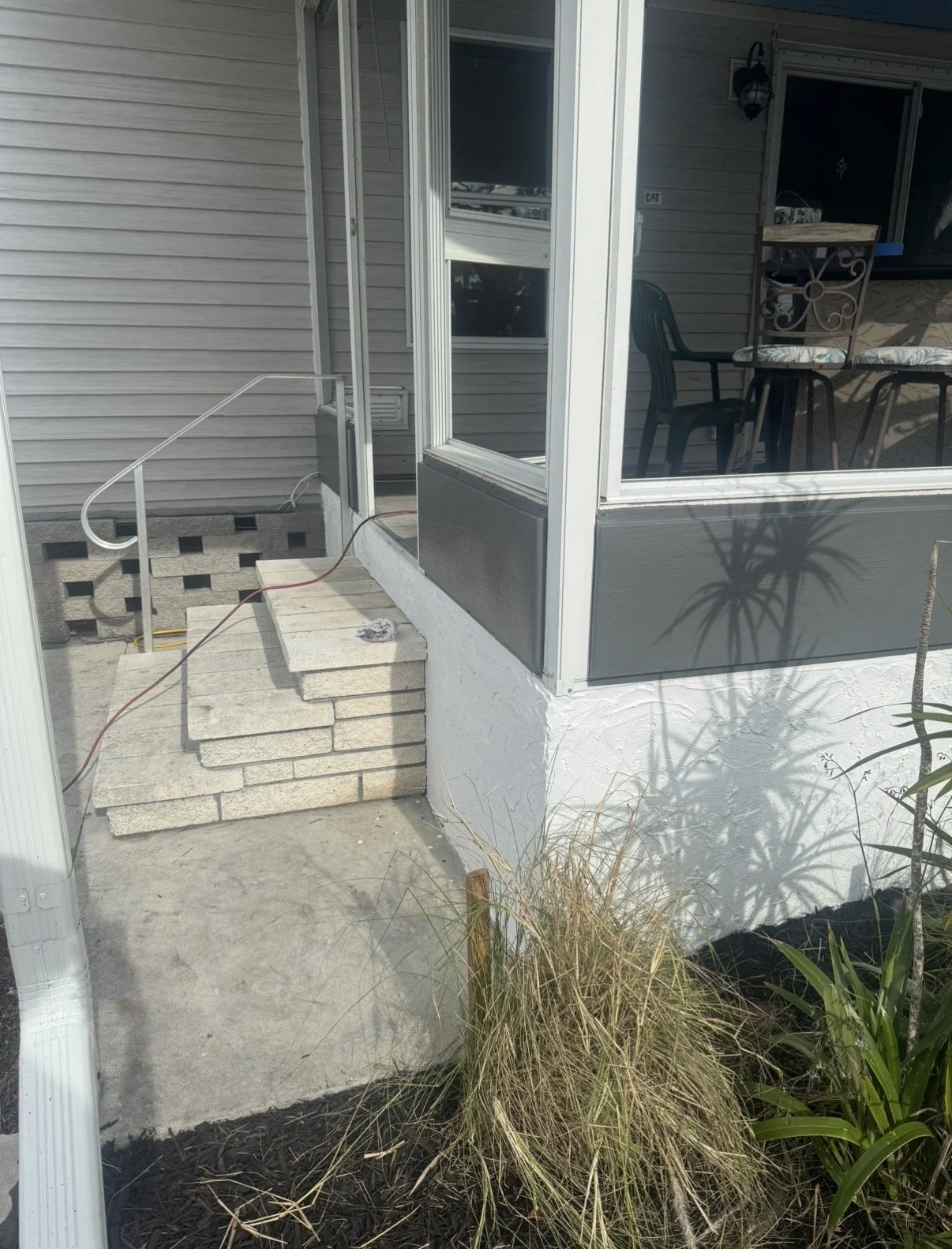 Partial view of a house porch with steps made of light-colored bricks, an area under construction, and a shadow of a potted plant on the wall.