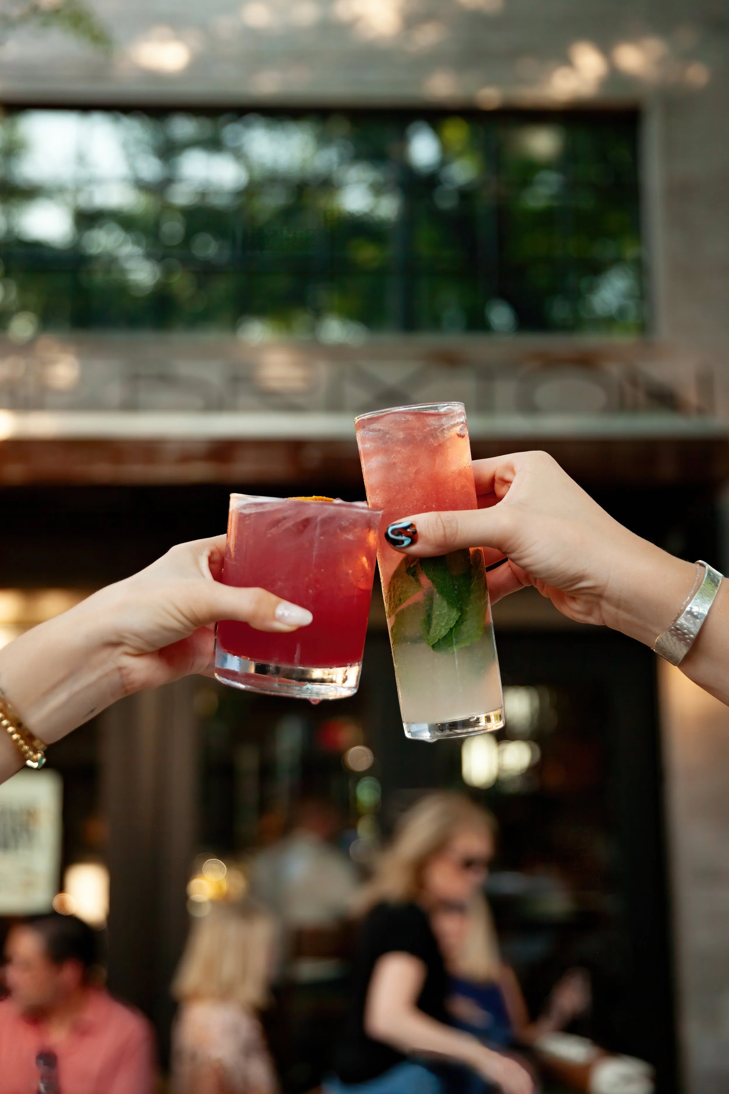 People raising celebratory drinks with a blurred background of guests at a social gathering.